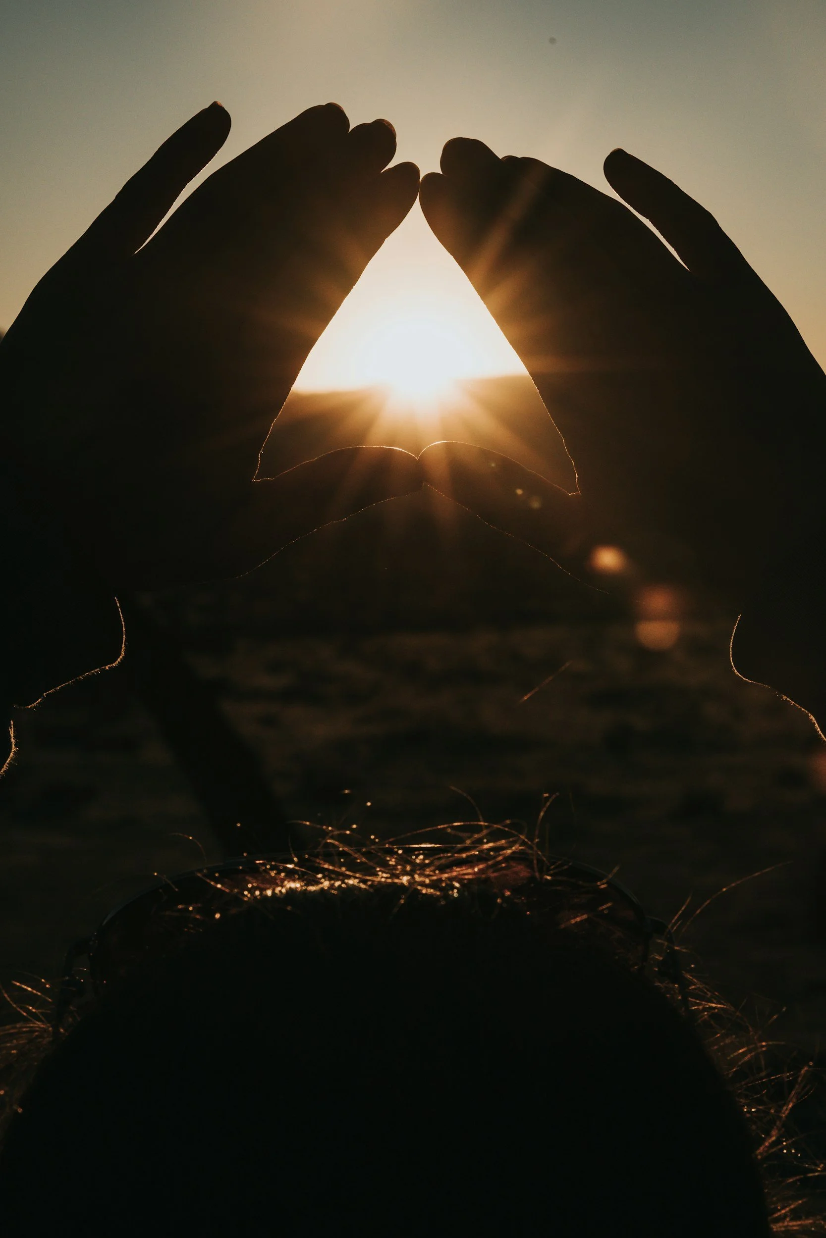 Silhouette of hands forming a heart shape around the setting sun at the beach.