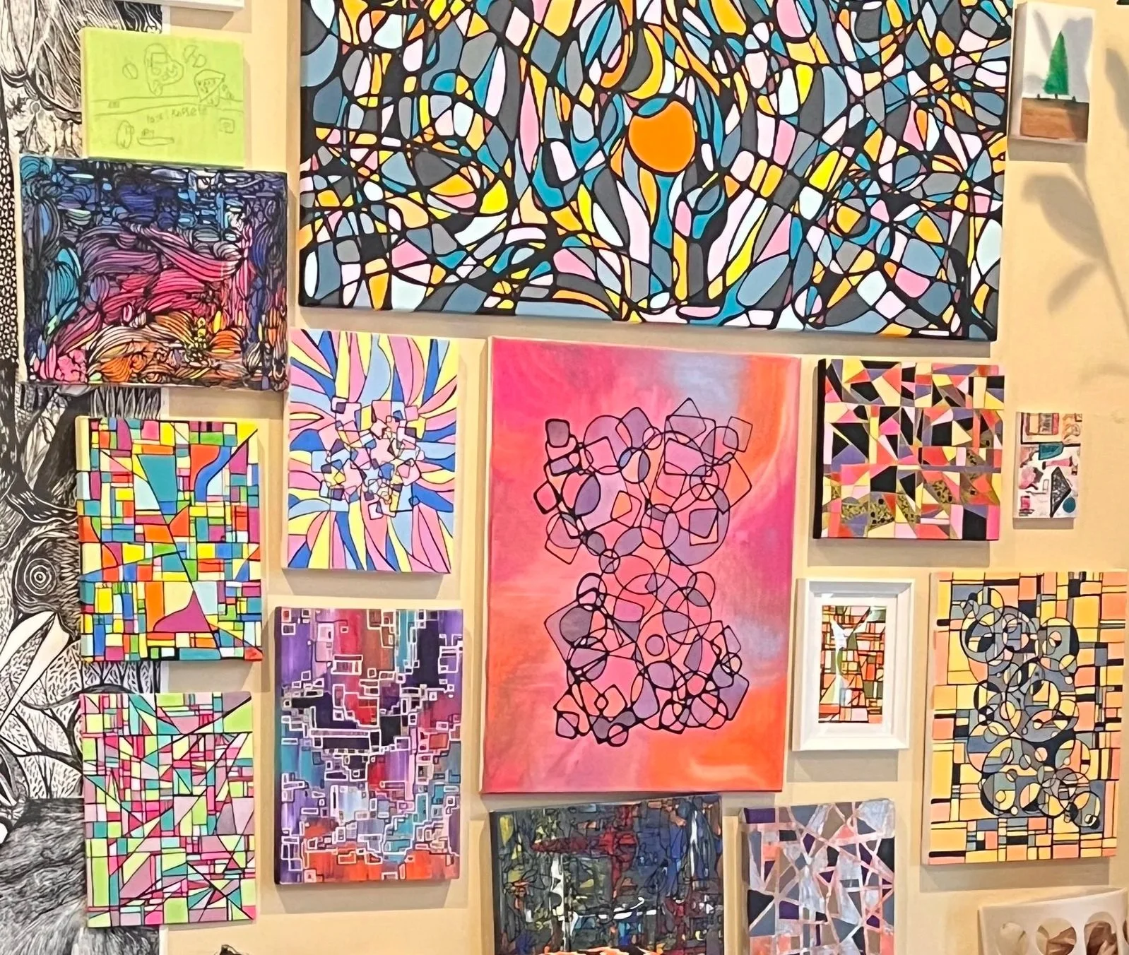 A gallery wall with various abstract paintings featuring bright colors and geometric patterns.
