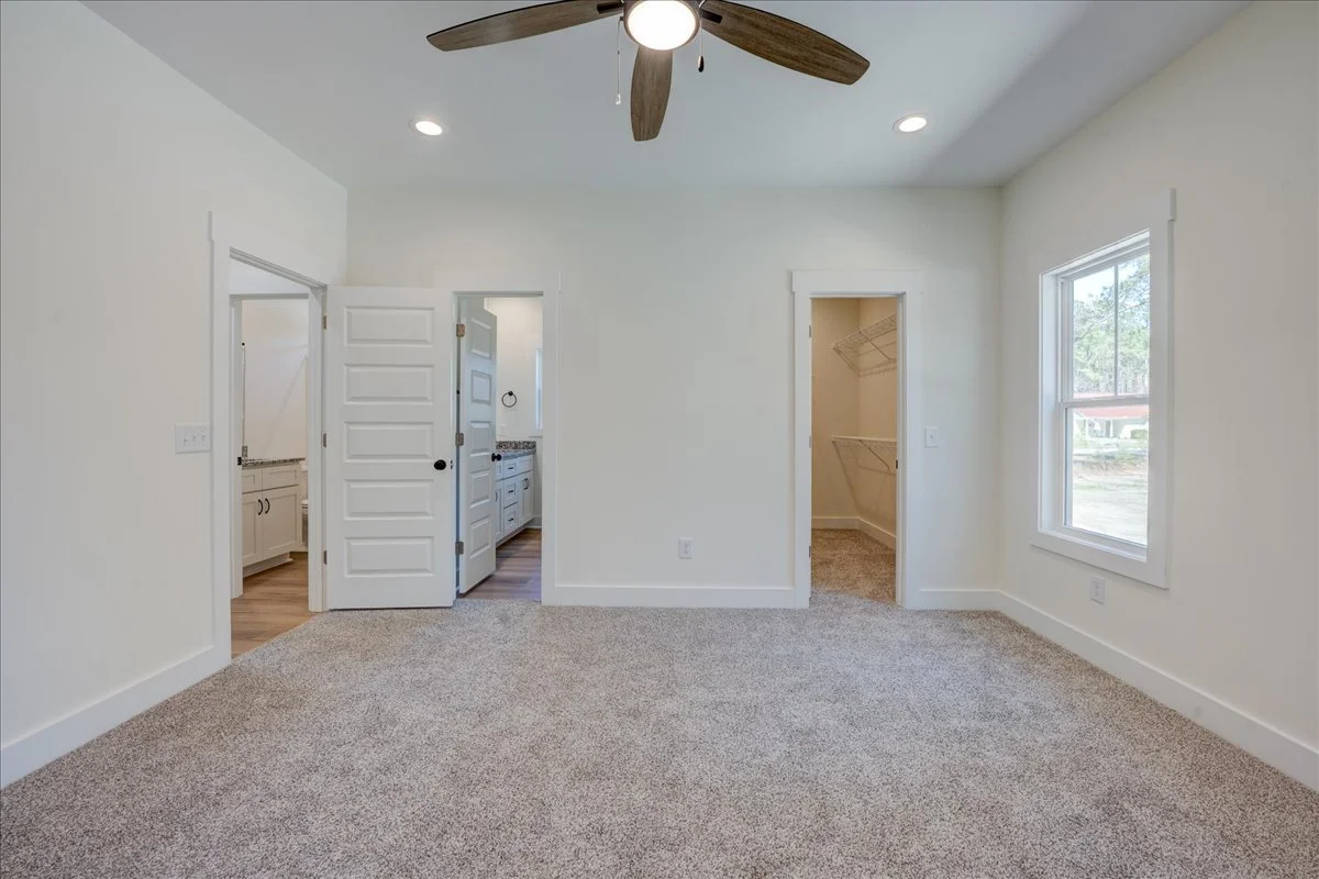 Empty bedroom with a ceiling fan, carpeted floor, and two windows, with two doors leading to a bathroom and walk-in closet.