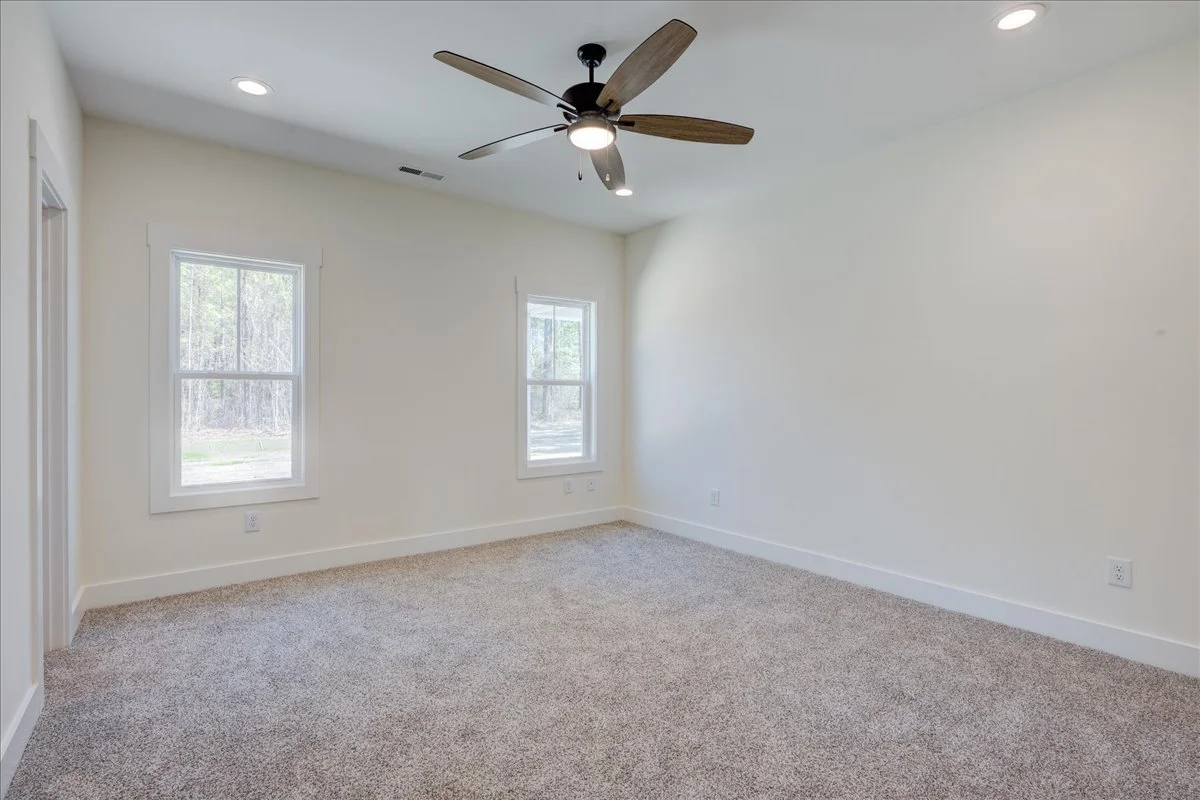 Empty bedroom with two windows, beige carpet, white walls, ceiling fan, and recessed lighting