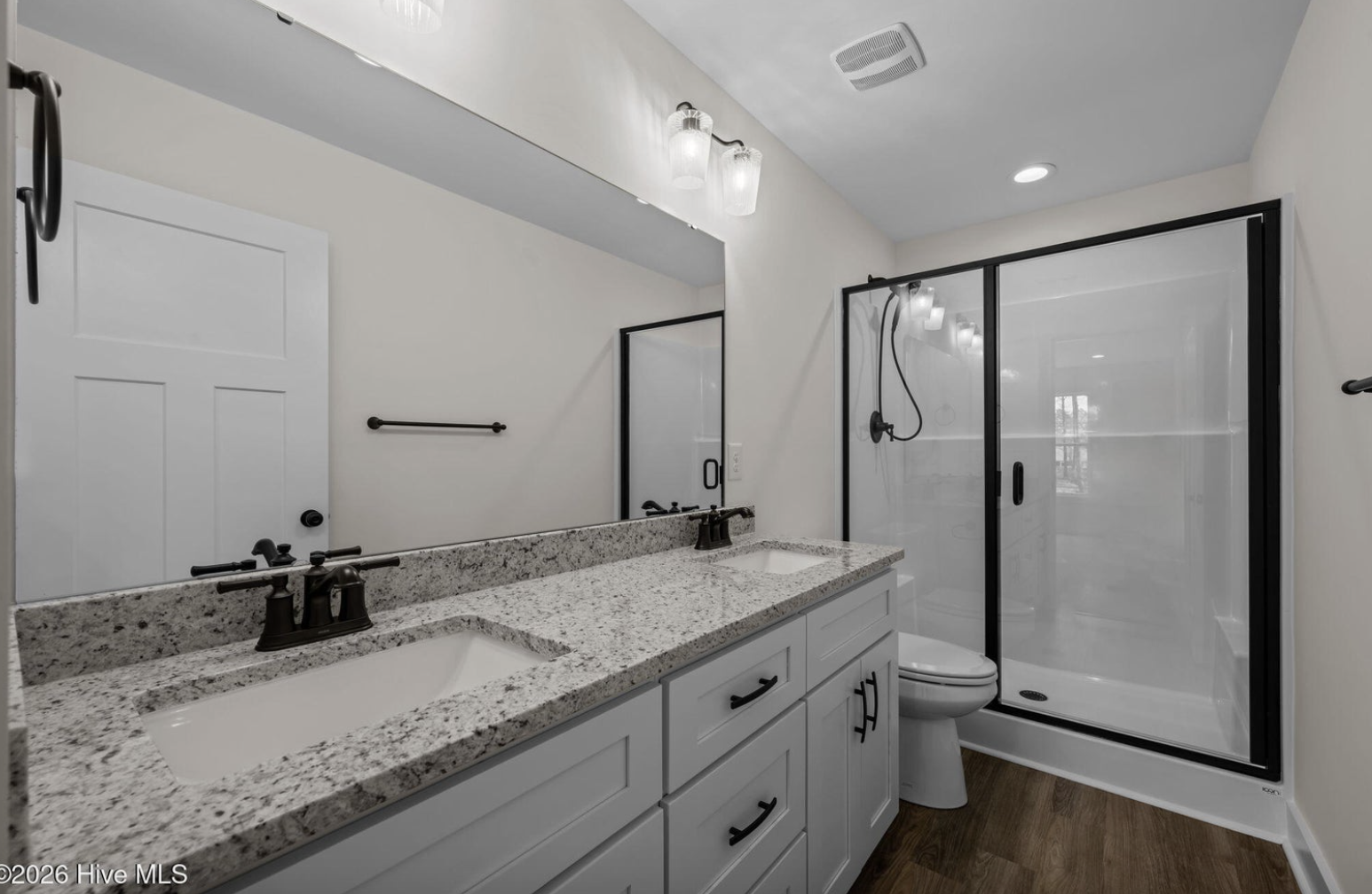 Bright modern bathroom with double vanity, granite countertops, black fixtures, and a large glass shower enclosure.