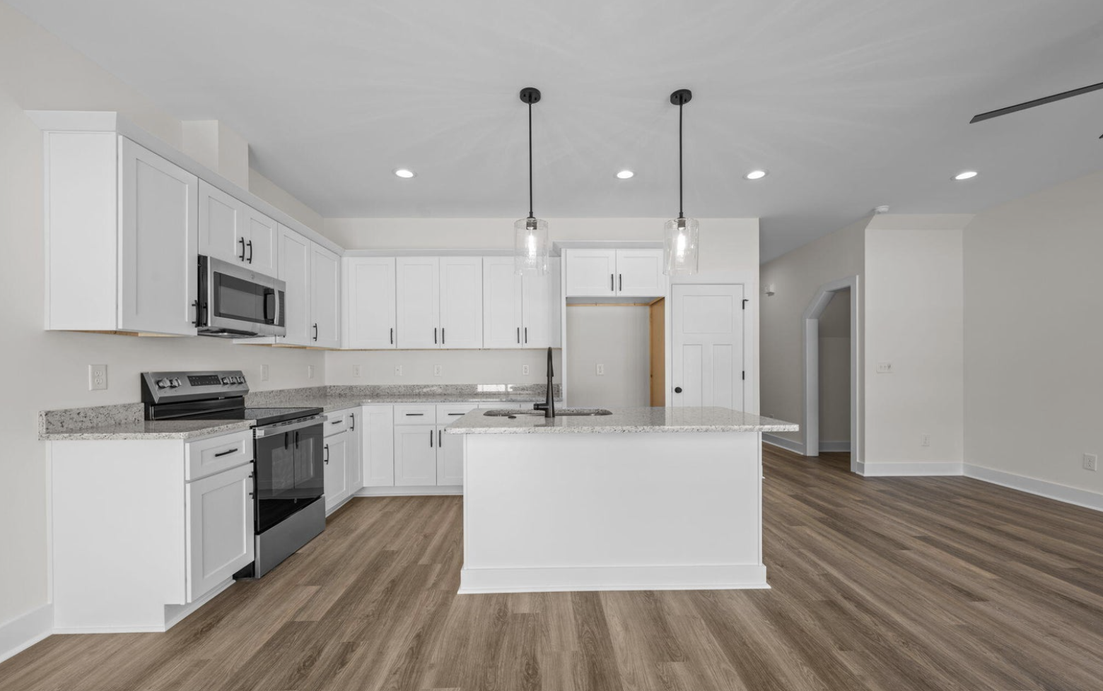 Modern kitchen with white cabinets, granite countertops, stainless steel appliances, pendant lighting, hardwood flooring, and an open layout.
