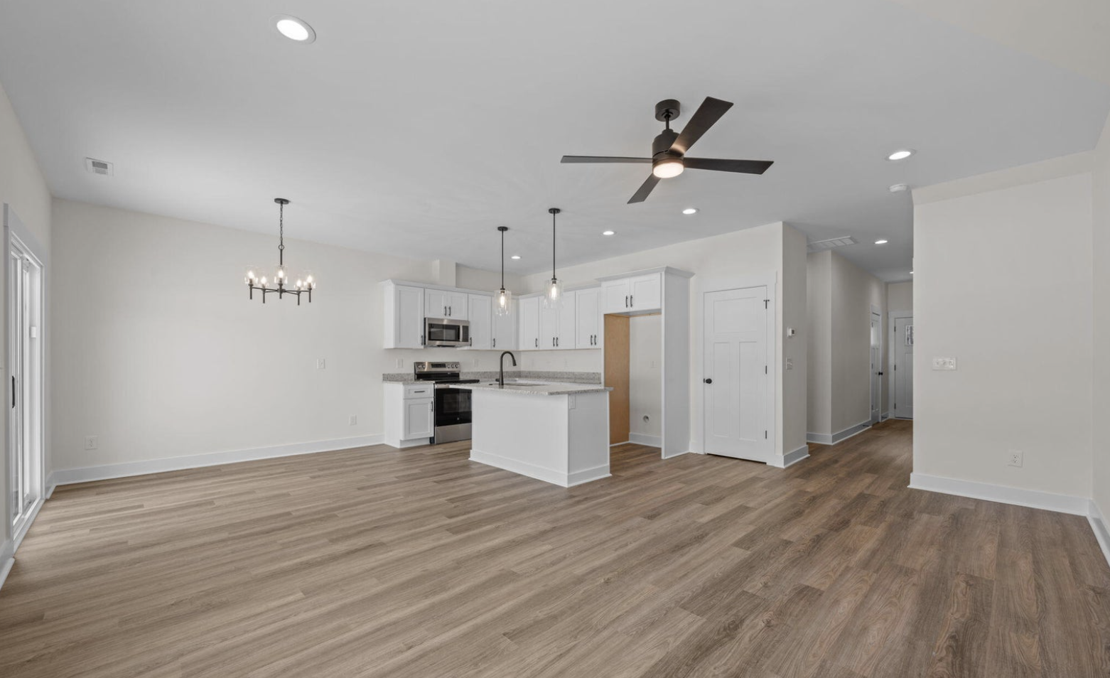 Open-concept living area with white kitchen cabinets, granite countertops, stainless steel appliances, wood flooring, ceiling fan, and pendant lights.