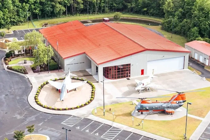An aerial view of a building with a red roof surrounded by aircraft displays and parking lot.