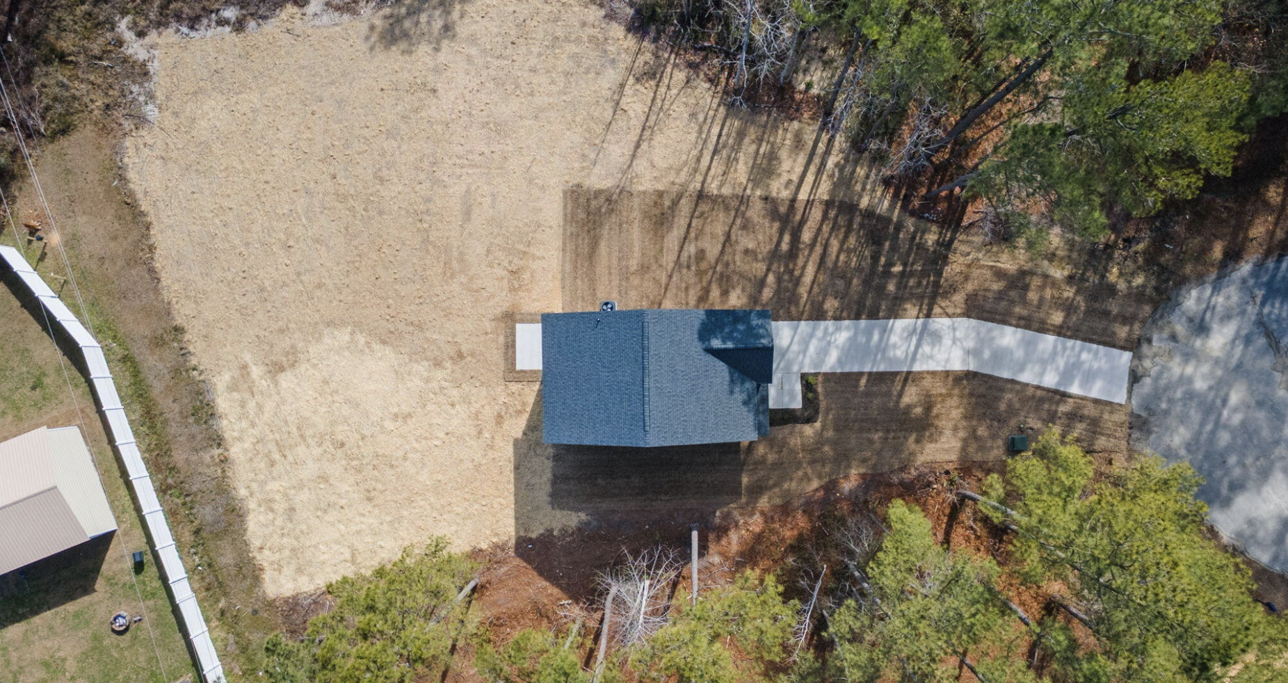 Aerial view of a small blue house with a driveway, surrounded by trees and open land in a rural area.