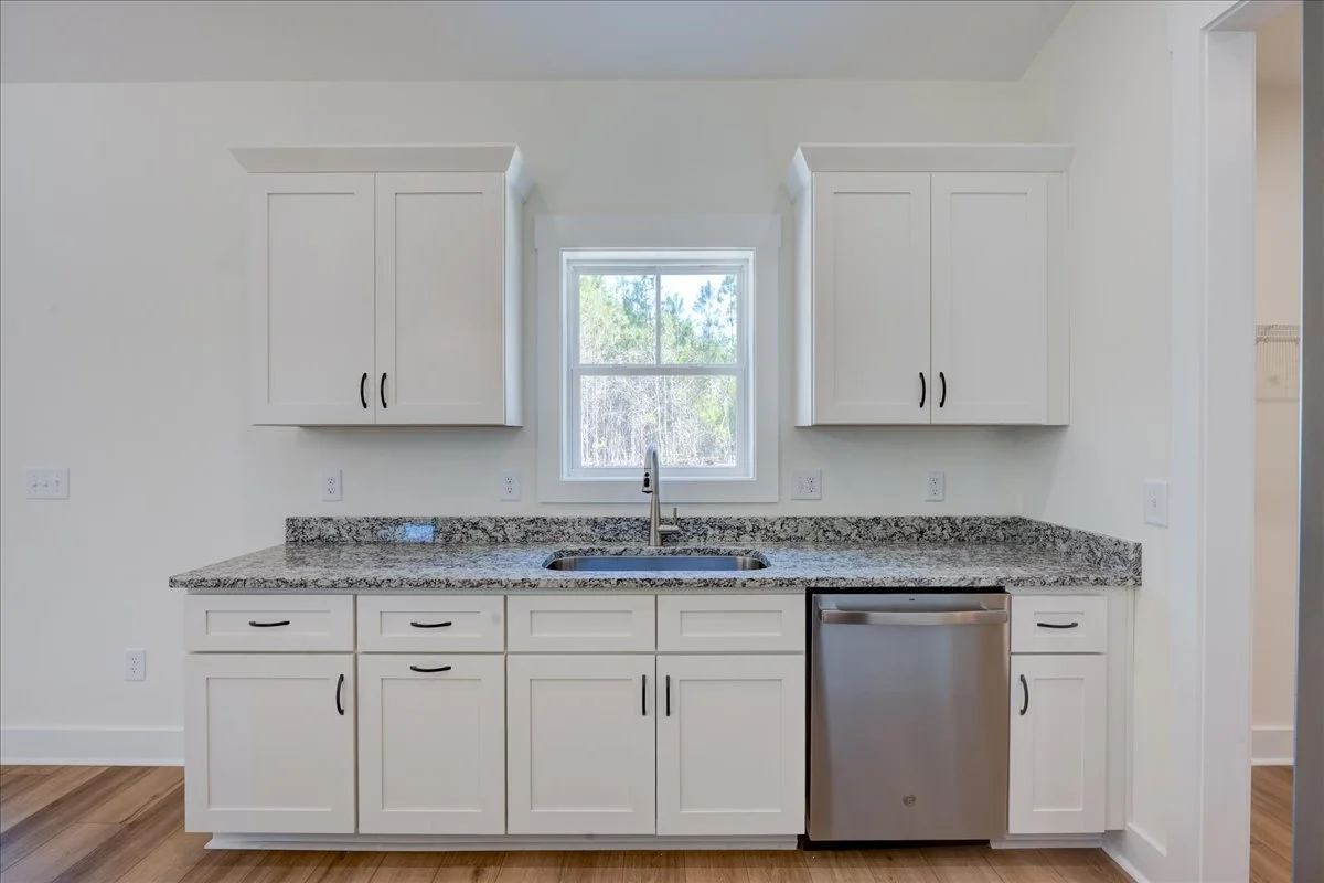 Kitchen with white cabinets, granite countertop, a window above the sink, and a stainless steel dishwasher.