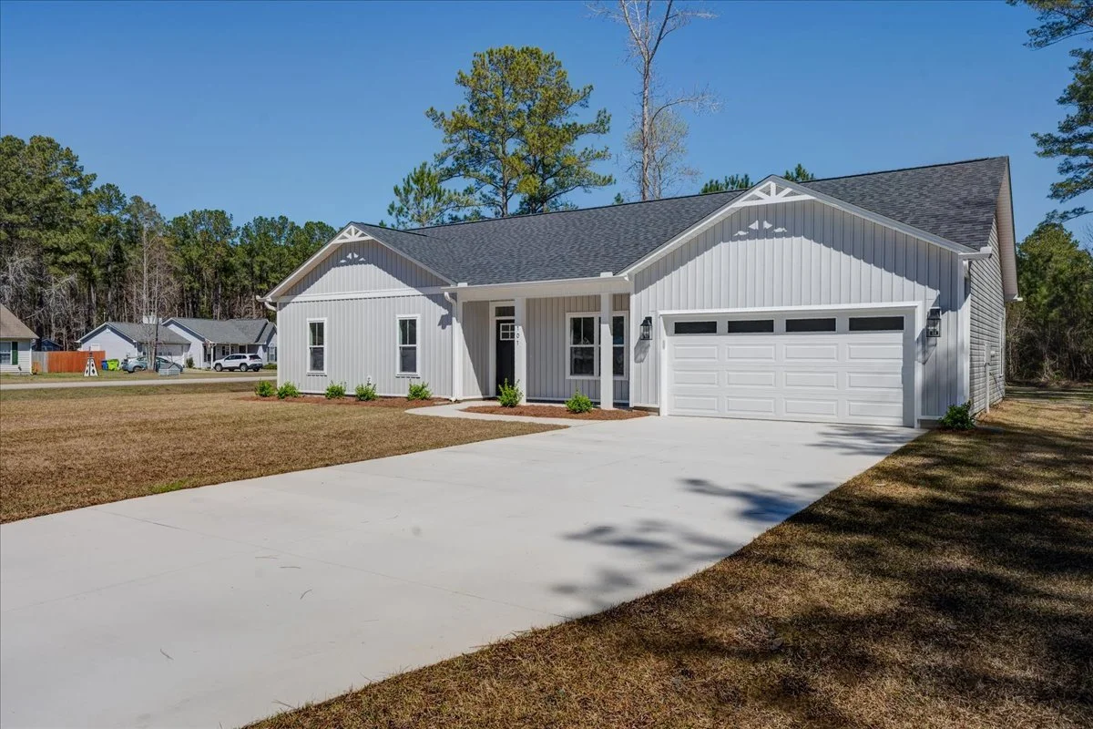 A newly built white house with a two-car garage, surrounded by a lawn and trees, with a concrete driveway leading to the garage.