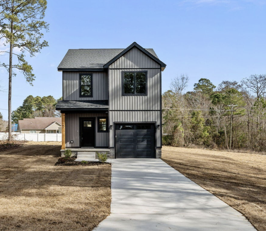 New two-story gray house with black trim and a garage, situated in a suburban area with a lawn and a paved driveway, under a clear blue sky.