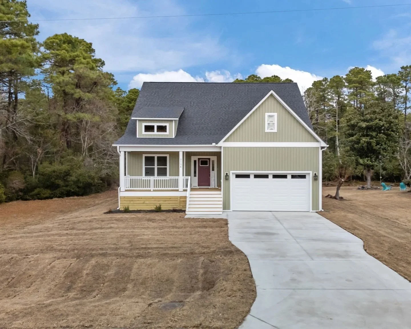 A two-story house with a light green exterior, a dark gray roof, white trim, and a white garage door, situated on a large grassy lot with a concrete driveway.