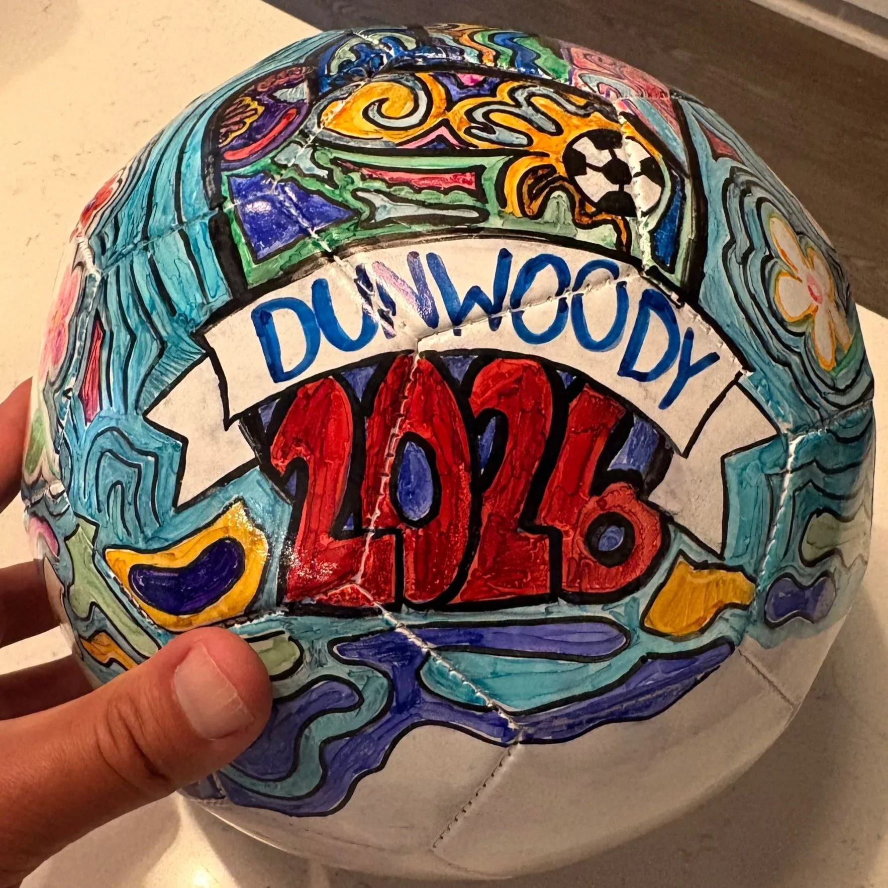 The Dunwoody DreamSphere 2026 by  Nathan and Adam Dinesman -  is a one-of-a-kind soccer ball that celebrates creativity, community, and the spirit of the game. Featuring vibrant hand-drawn artwork, flowing blue patterns, colorful floral accents, and 