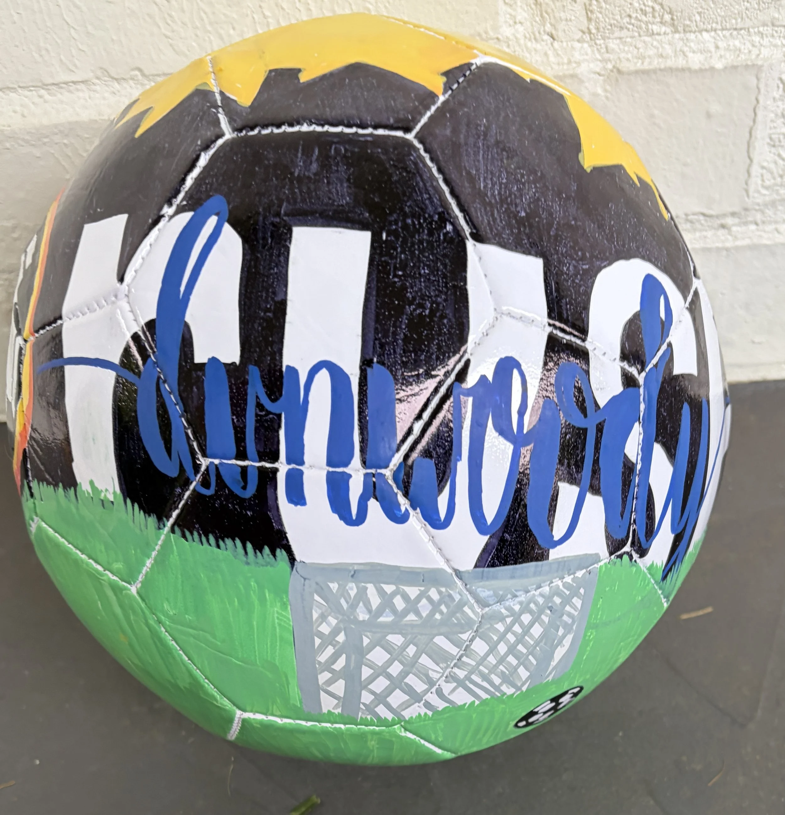 City of Champions (front) by Linley McGukin: My artwork represents how sports bring a city together. The skyline, field, and soccer elements symbolize teamwork, dedication, and the dreams that inspire athletes to become champions both on and off the 