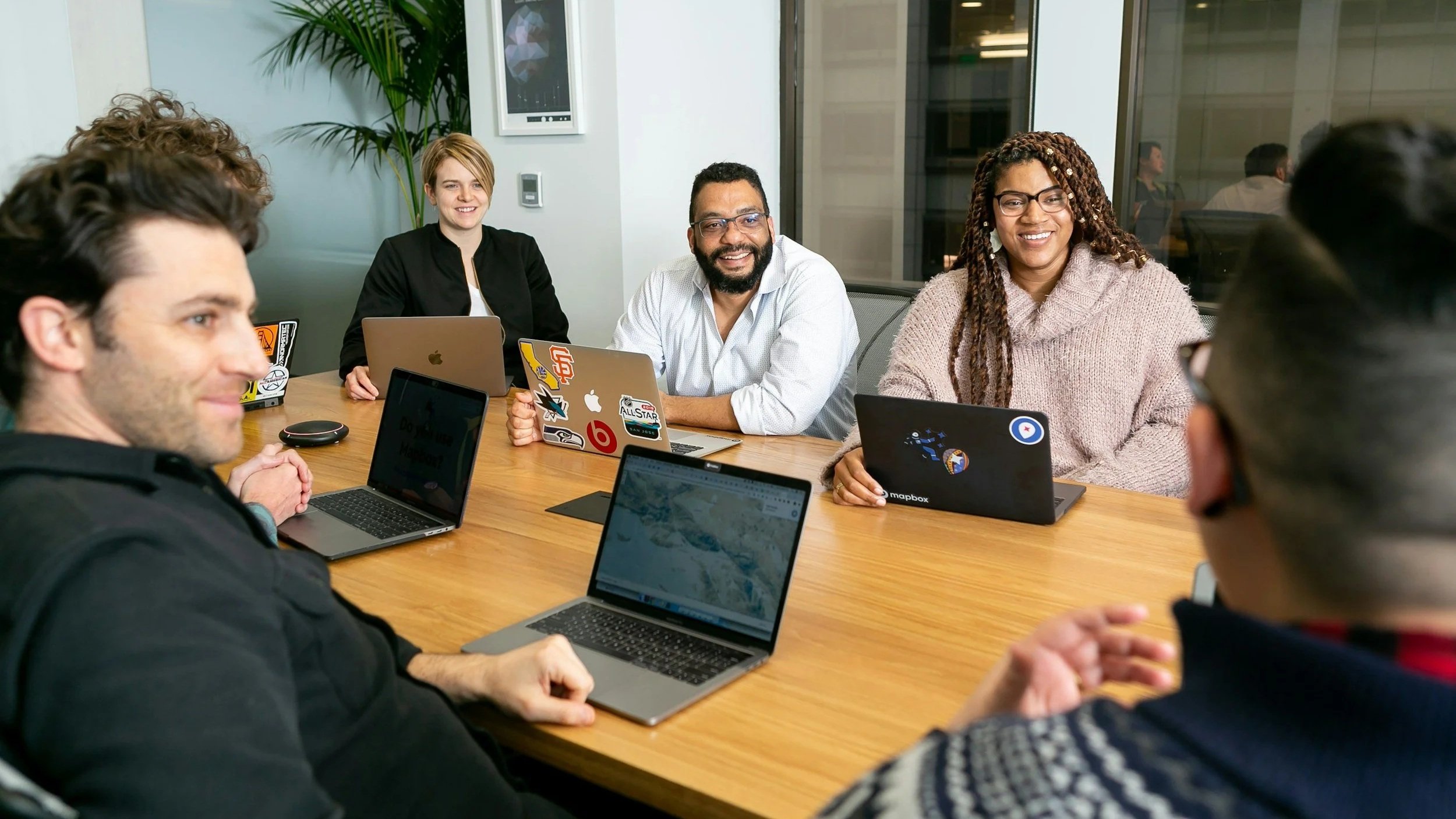 several people of various ethnic backgrounds sitting around a conference table smiling in the direction of one individual partially out of view