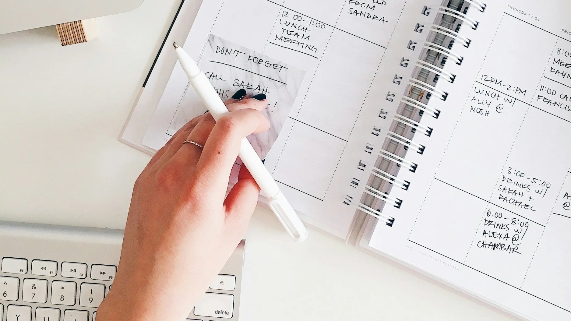 A persons hand, holding a pen, over an open weekly planner with daily tasks filled in.