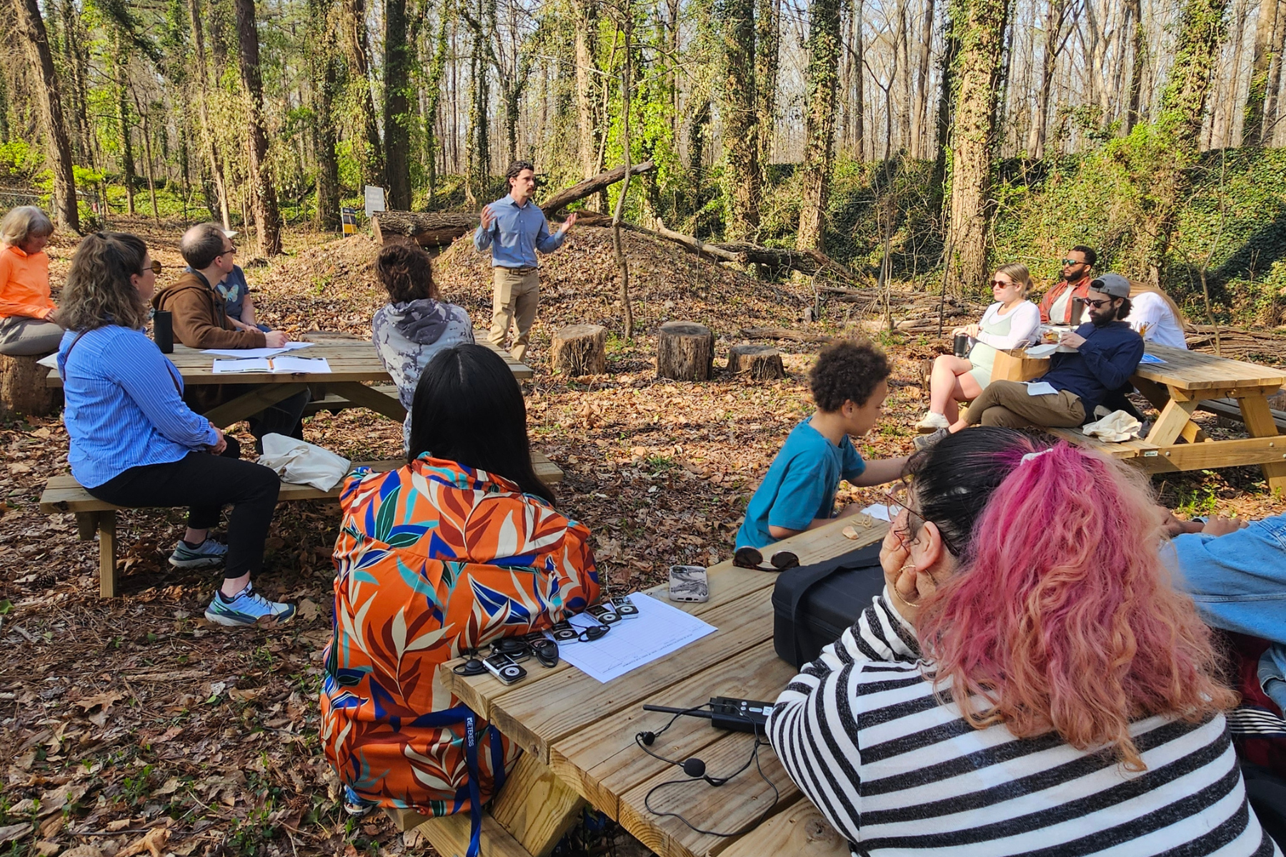 Community members gather around picnic tables under the canopy at Ernest Road Park for an outdoor learning classroom.