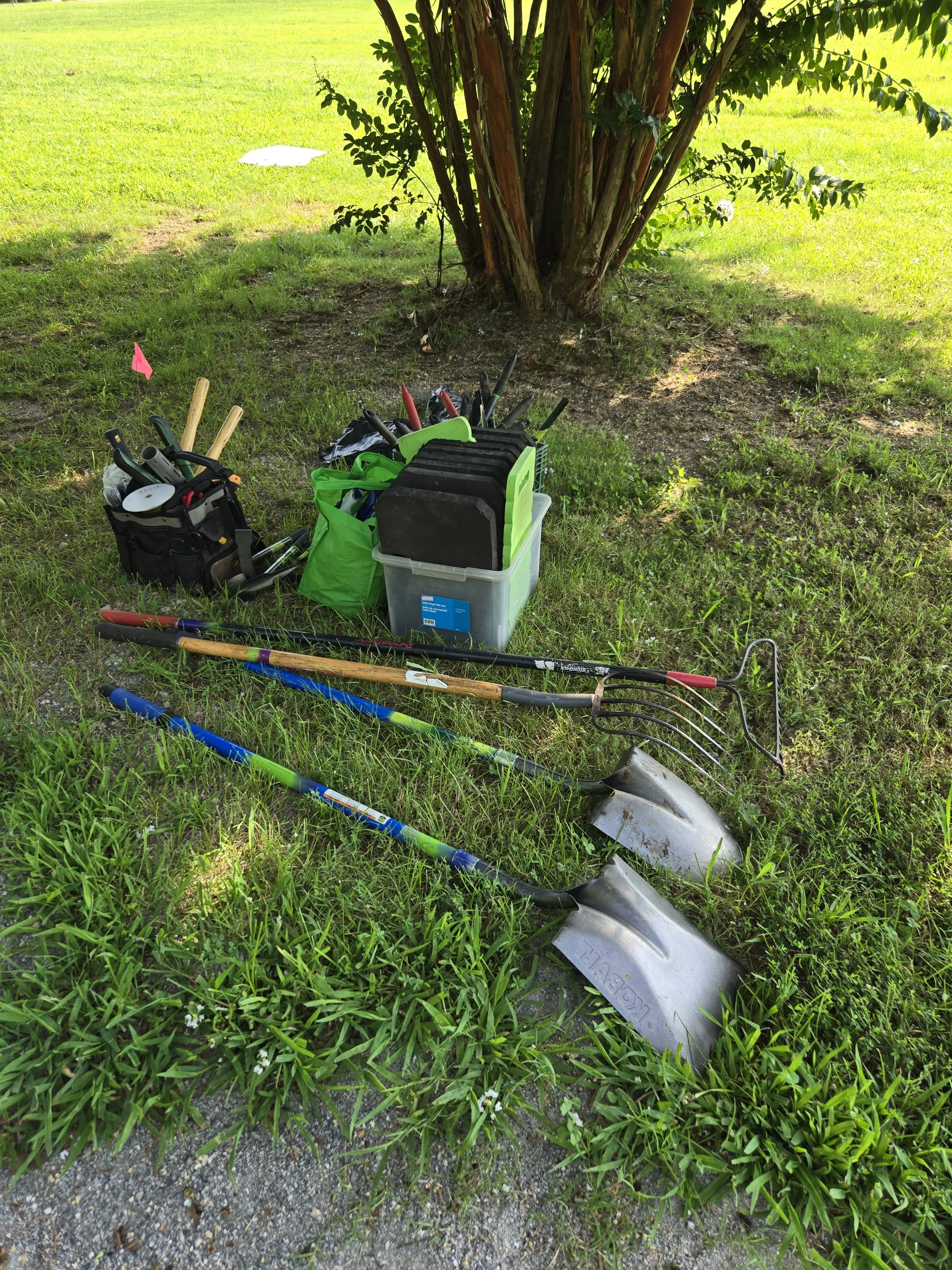 Tools, including shovels, rakes, and bins full of smaller tools sit on the grass at Canoe Run Park