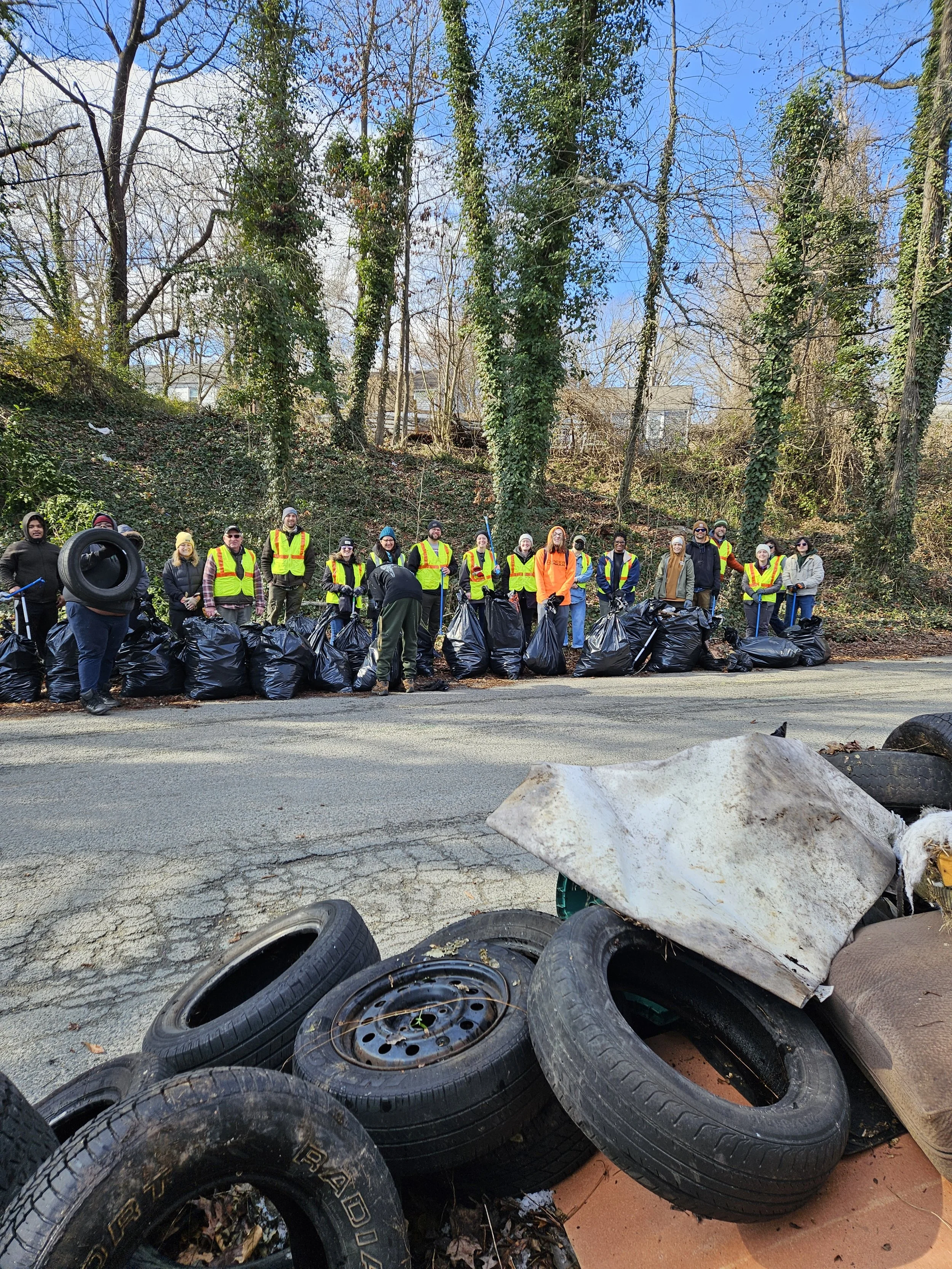 A large group of volunteers wearing safety vests pose with the pile of tires and bags of trash they cleaned up along Ernest Road during a service day to honor Martin Luther King Jr.