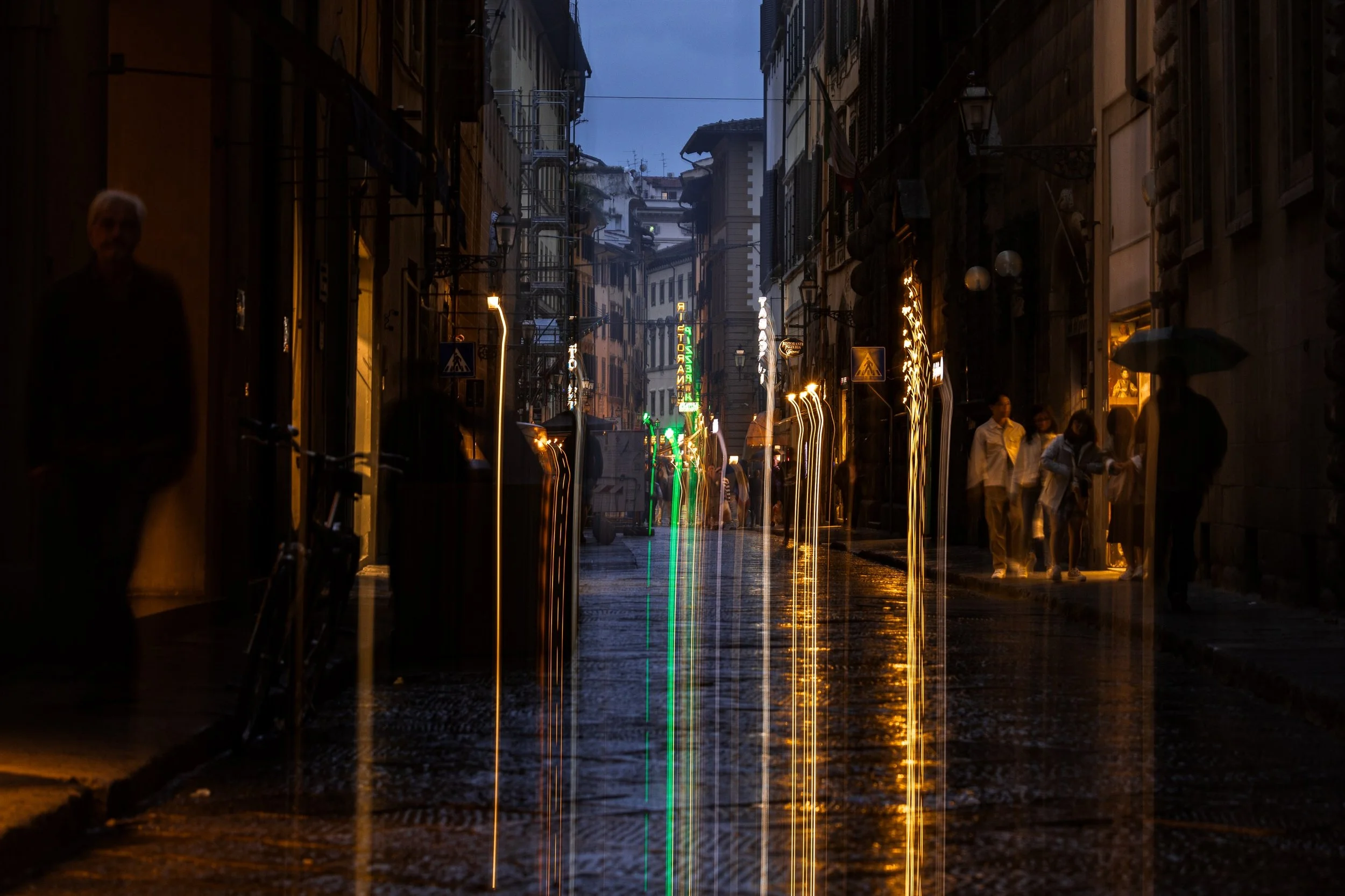 Rain-darkened Florence street at night with pedestrians, amber lamps, and green and gold light trails