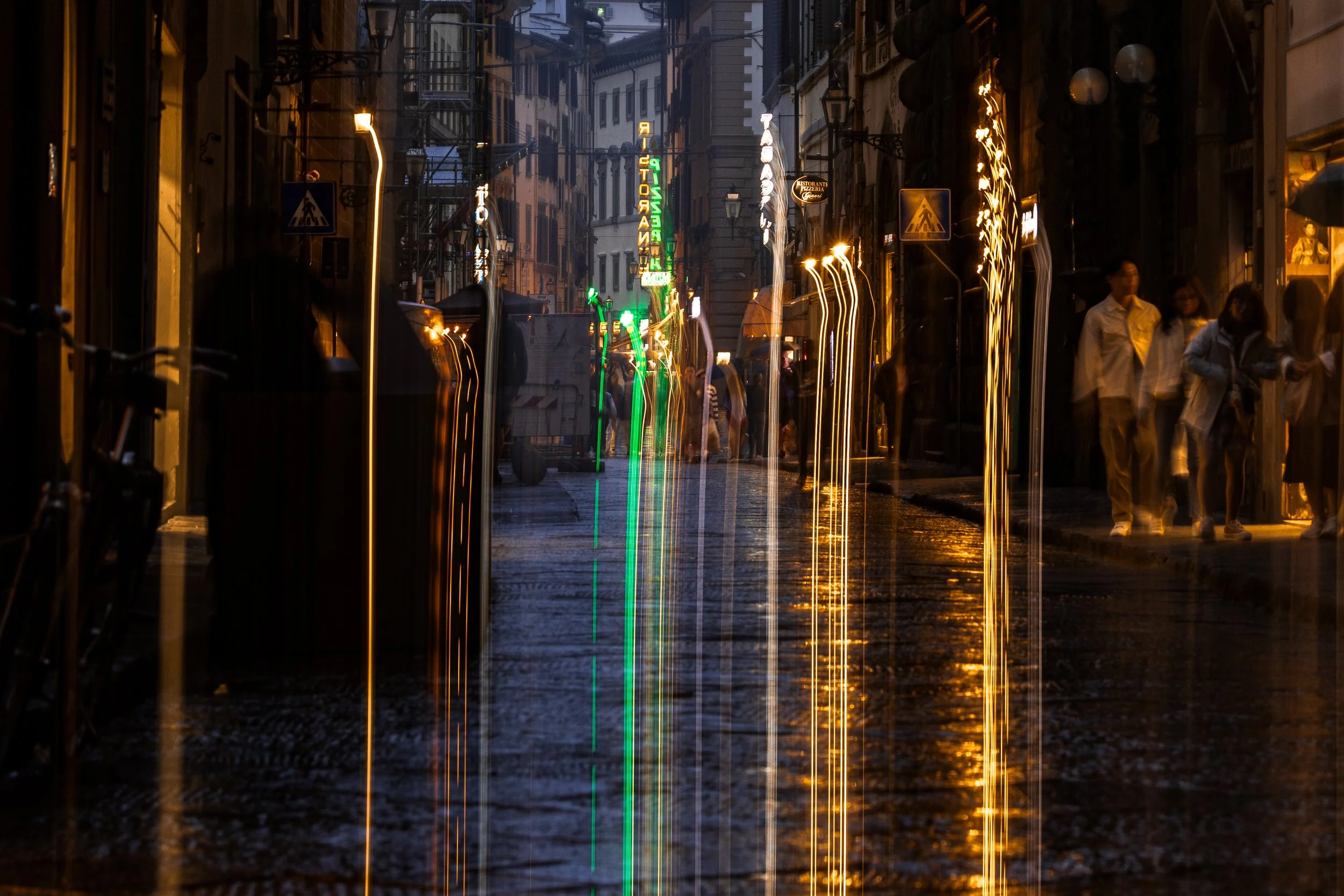 Close detail of reflected light trails and softly moving pedestrians along the narrow Florence street