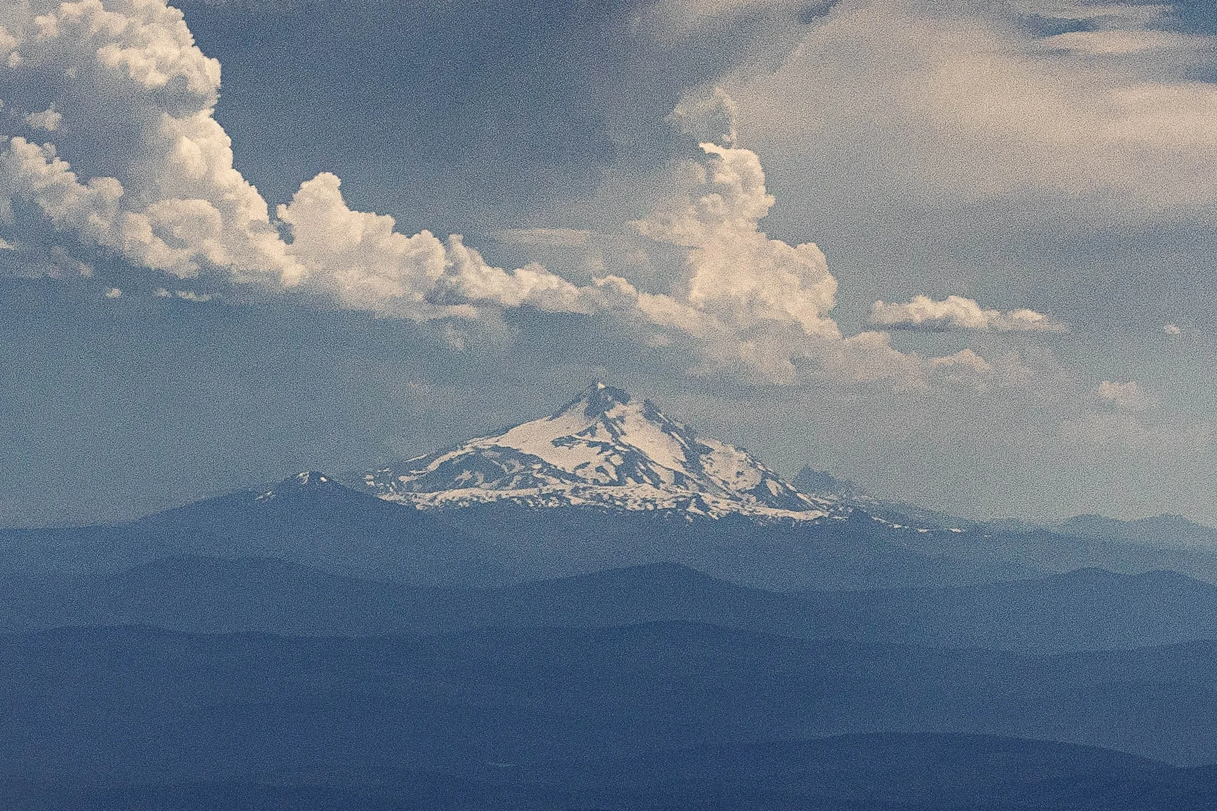 Distant Mount Jefferson beneath large summer clouds and layered blue ridgelines