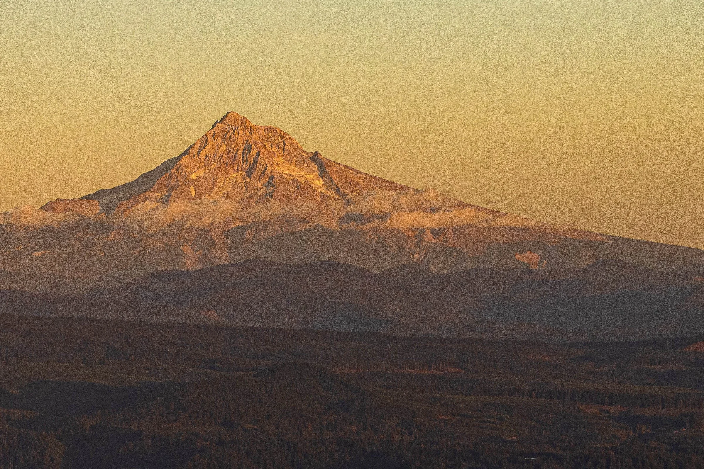Close detail of Mount Hood in warm evening light above layered forest ridges