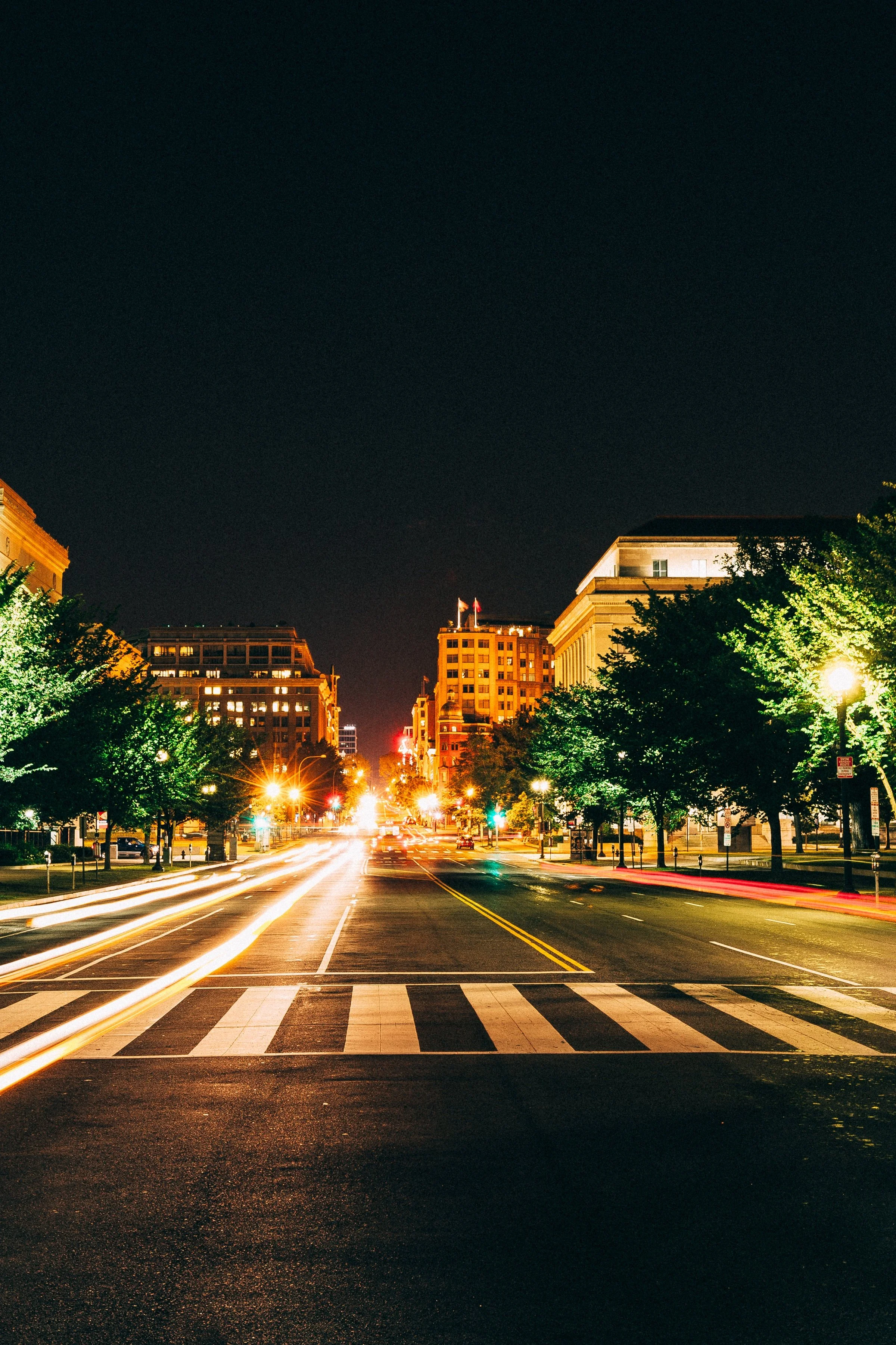 Vertical detail of light trails crossing an empty foreground toward illuminated buildings at the end of the avenue