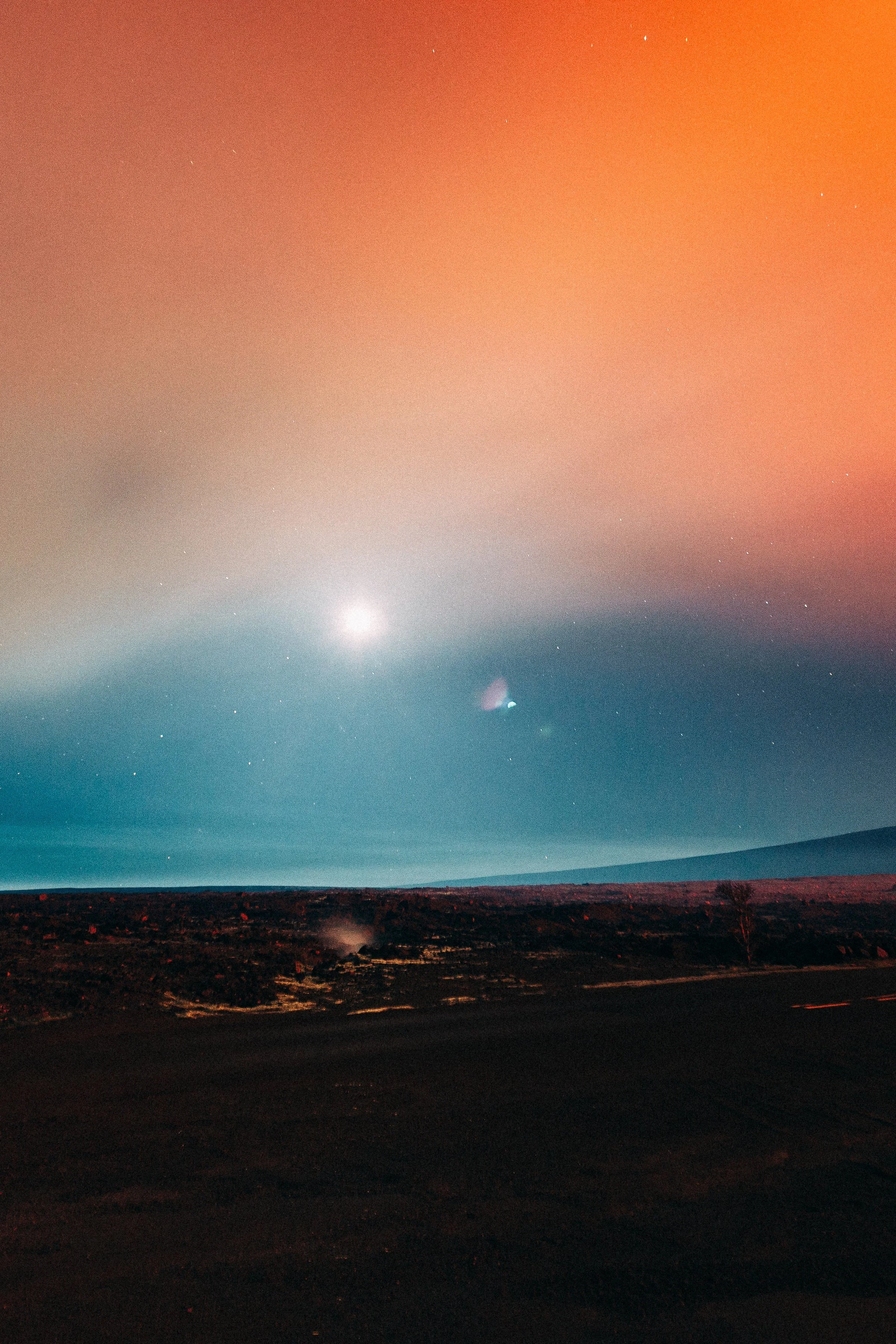 Vertical detail of the moon, colored haze, dark volcanic ground, and a thin red road trail