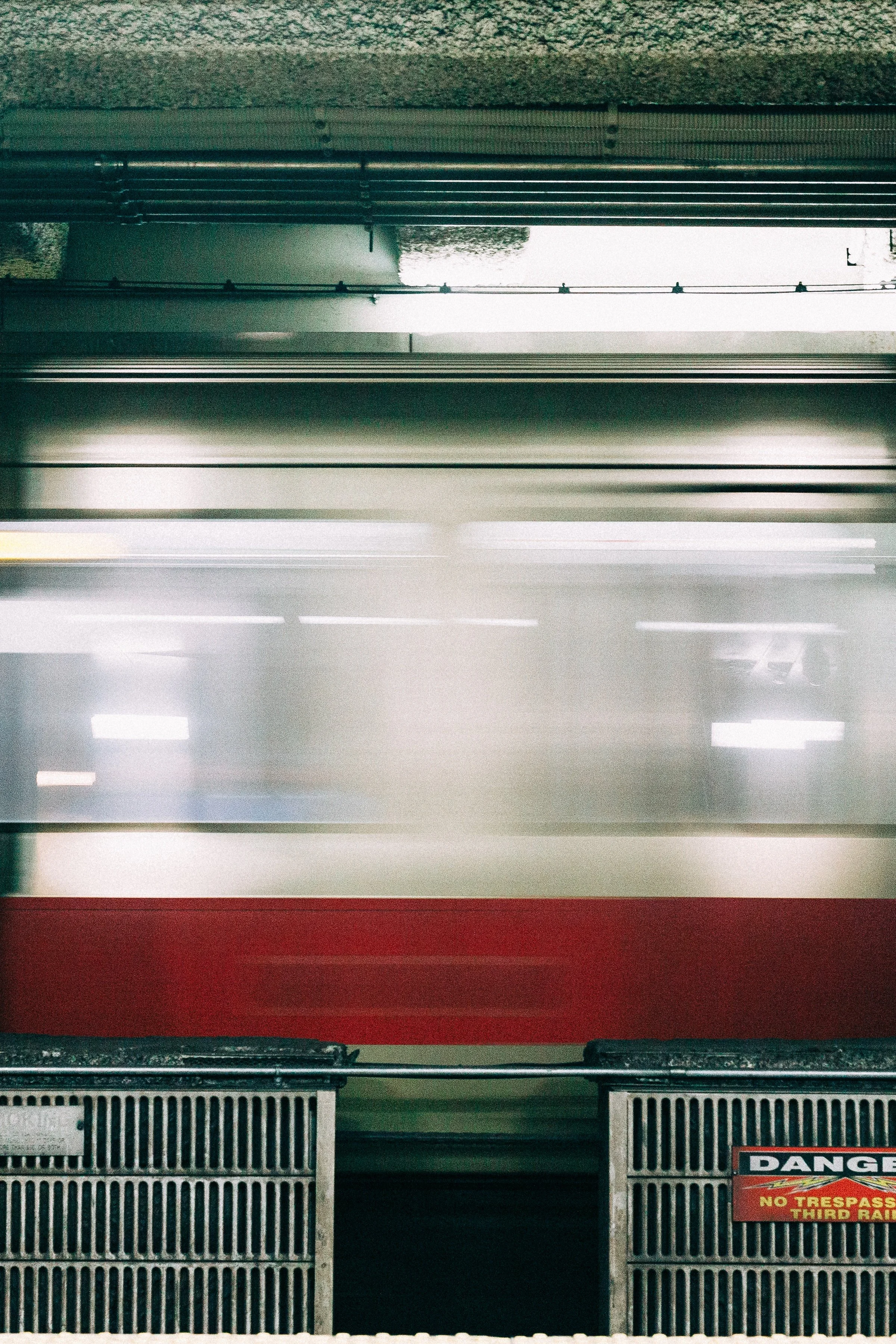 Vertical detail of the moving train framed by concrete columns, railing, and platform signs