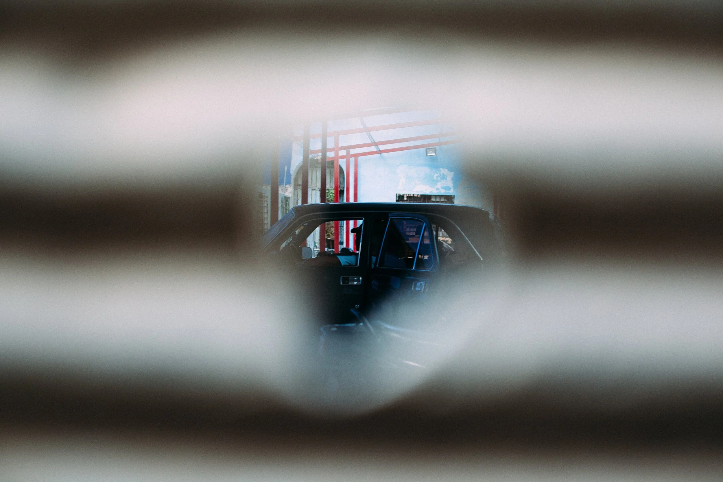 Partially obscured scene with colorful architecture seen through narrow openings in a pale fence