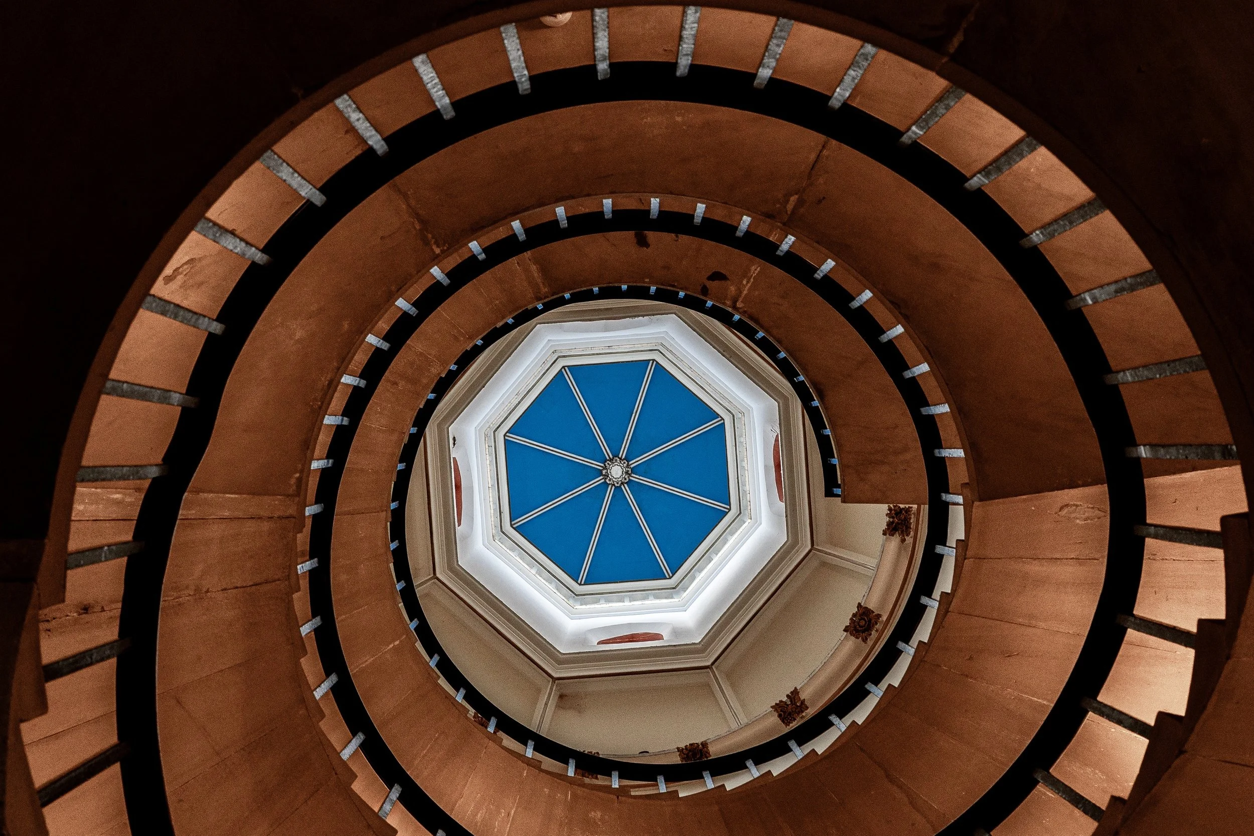 Close detail of curved railings, pale stair edges, and the blue skylight at the center