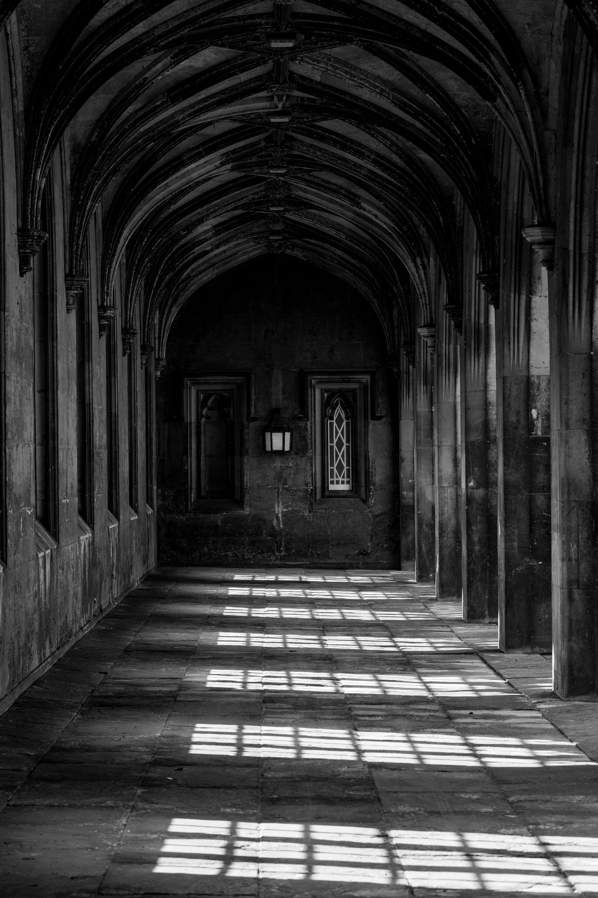 Vertical black-and-white view through repeating pointed arches with rectangular window light across the floor
