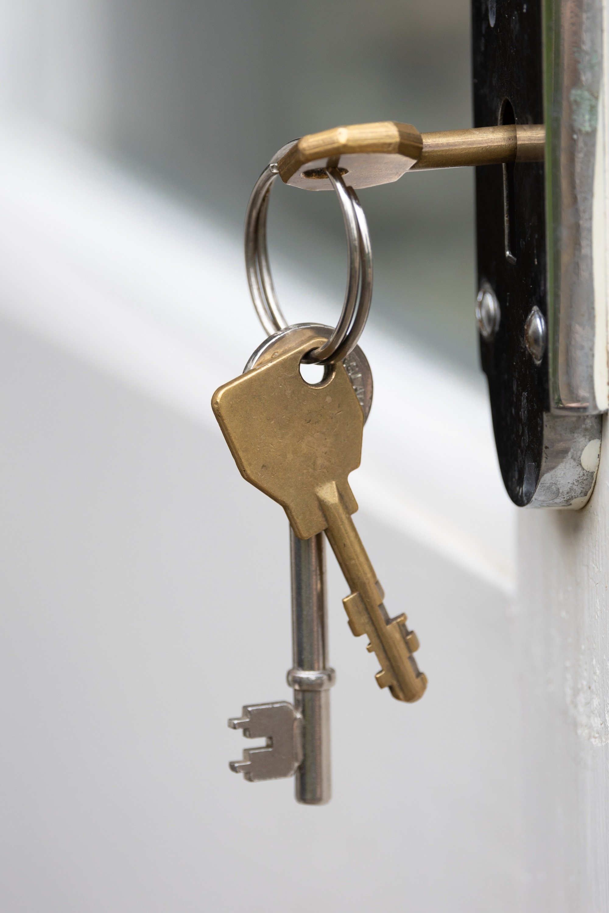 Two worn European keys hanging from a ring attached to a third key inserted into a brass door lock
