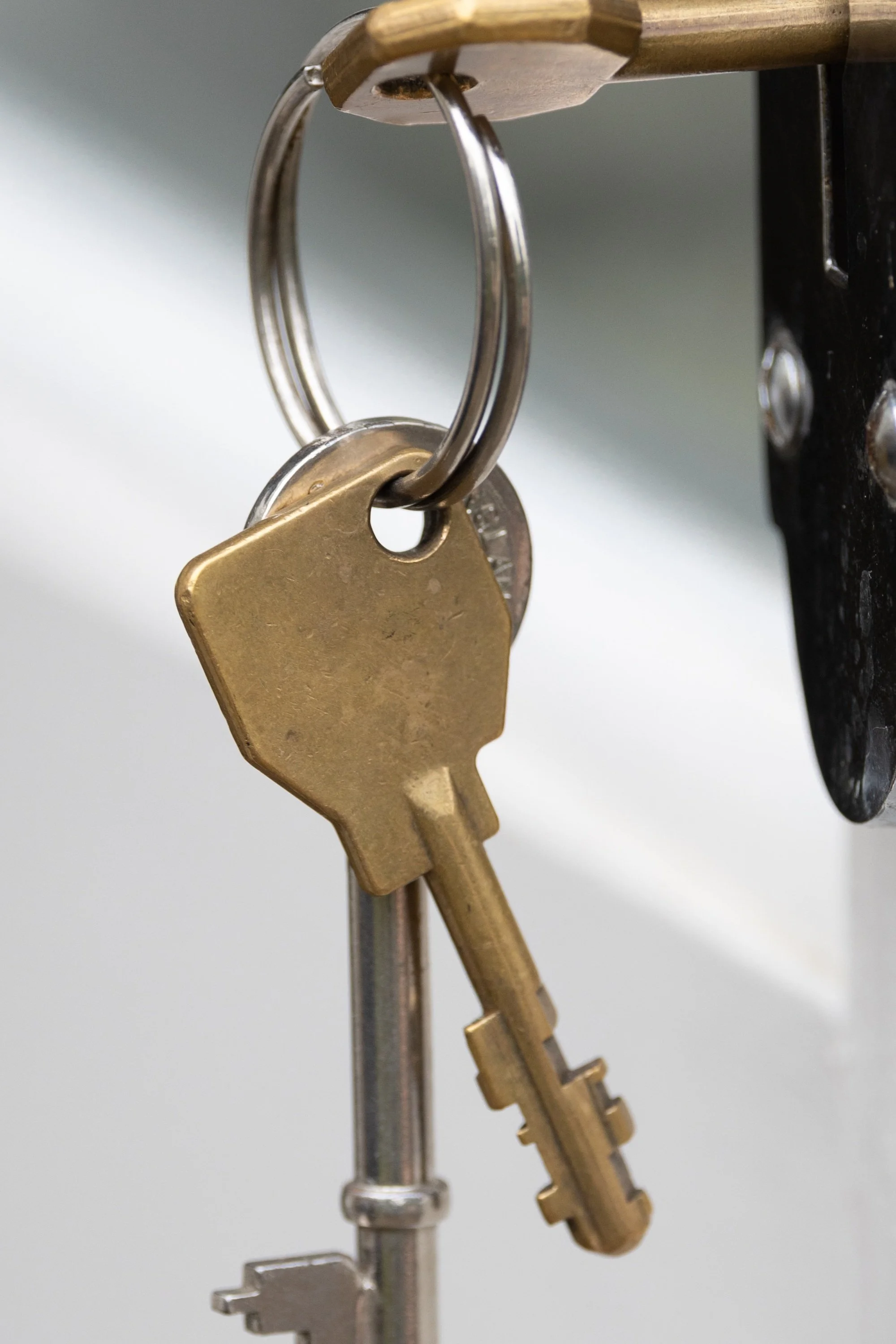 Close detail of three keys, the metal ring, brass lock, worn surfaces, and black door hardware