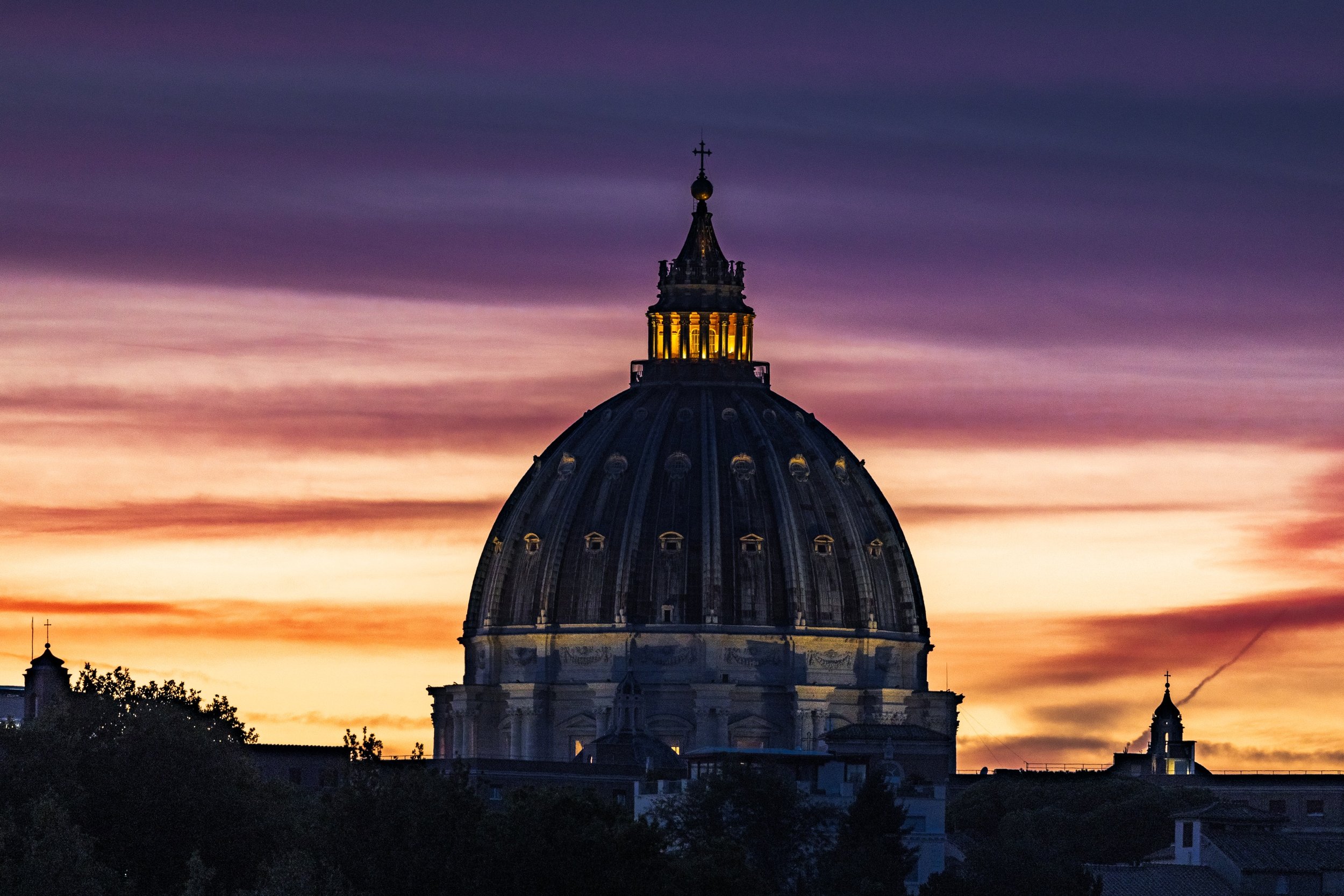 Dome of St. Peter's Basilica silhouetted beneath amber, rose, and violet evening clouds in Vatican City