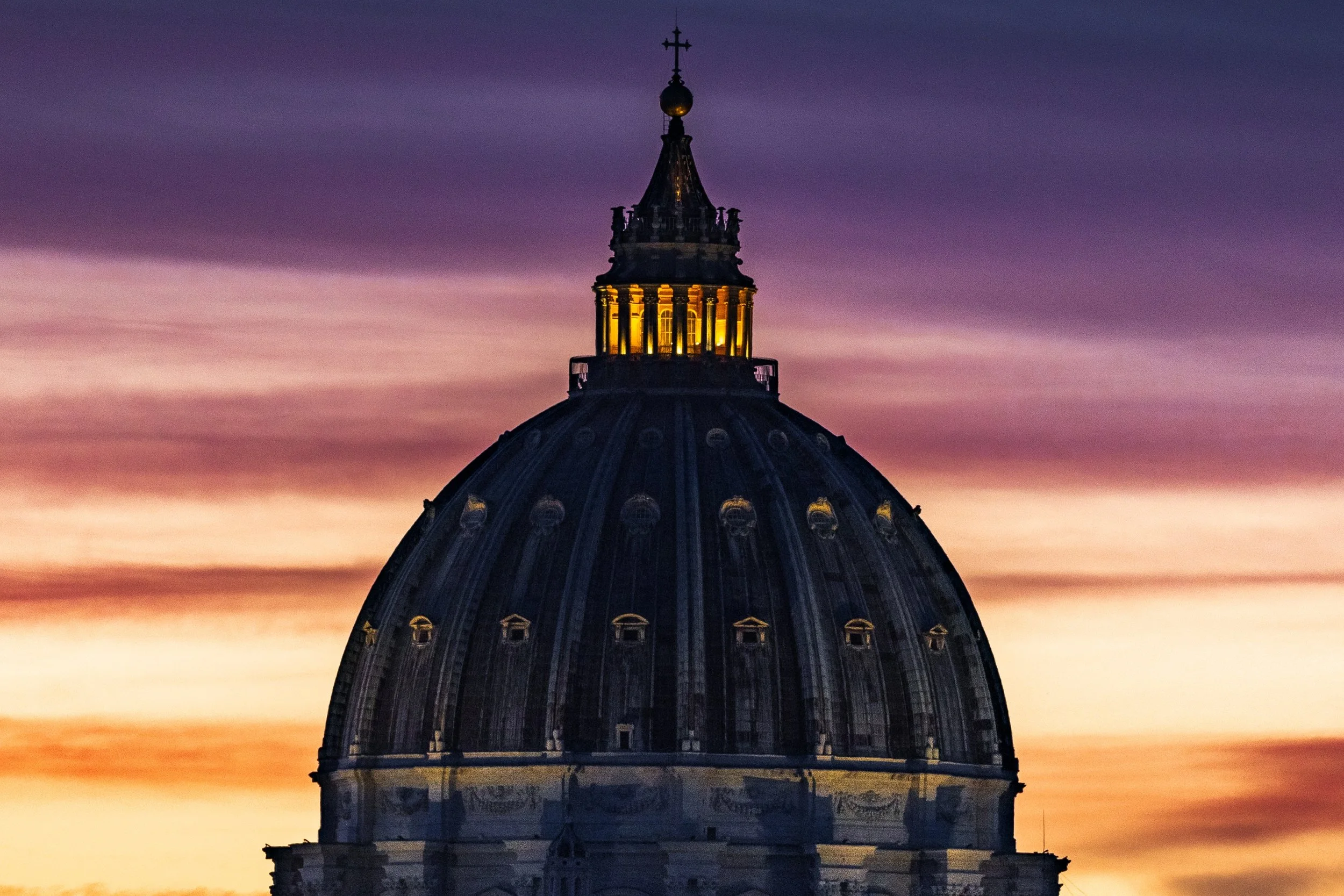 Close detail of the illuminated lantern and ribbed dome of St. Peter's Basilica against the dusk sky