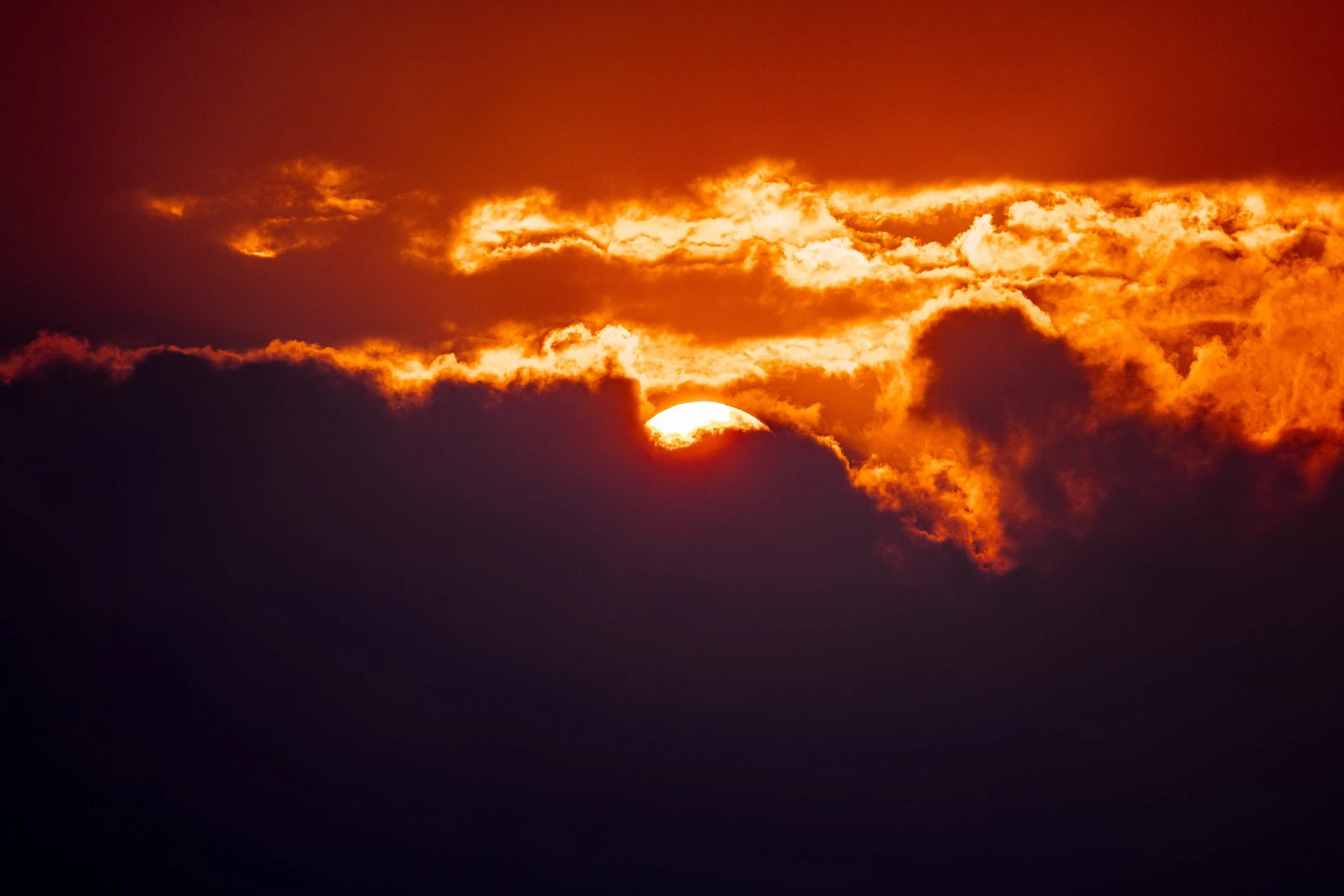 Partial sun glowing through fiery orange clouds above a broad field of violet shadow