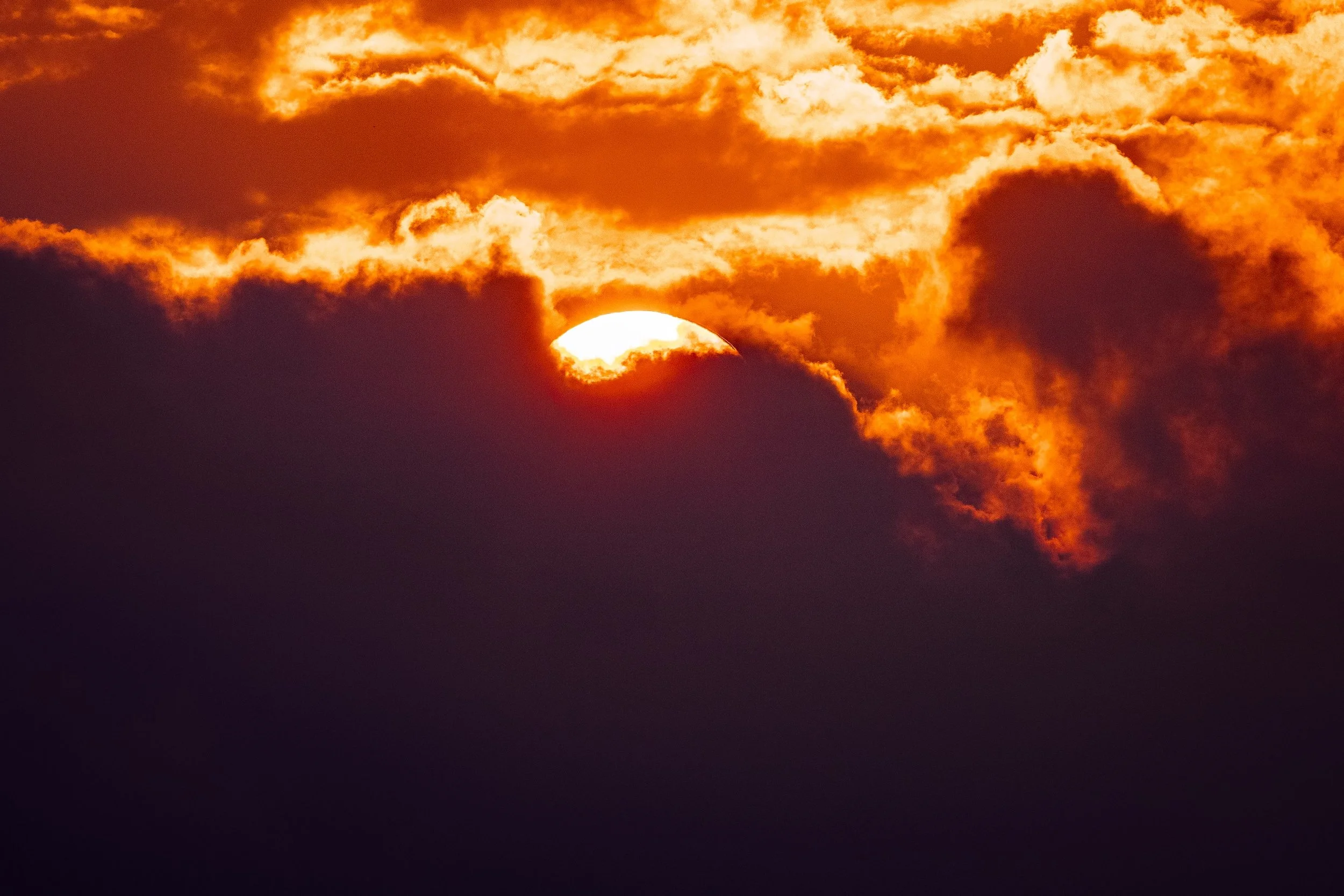 Close detail of the sun, illuminated cloud edges, dark vapor, and saturated orange sky