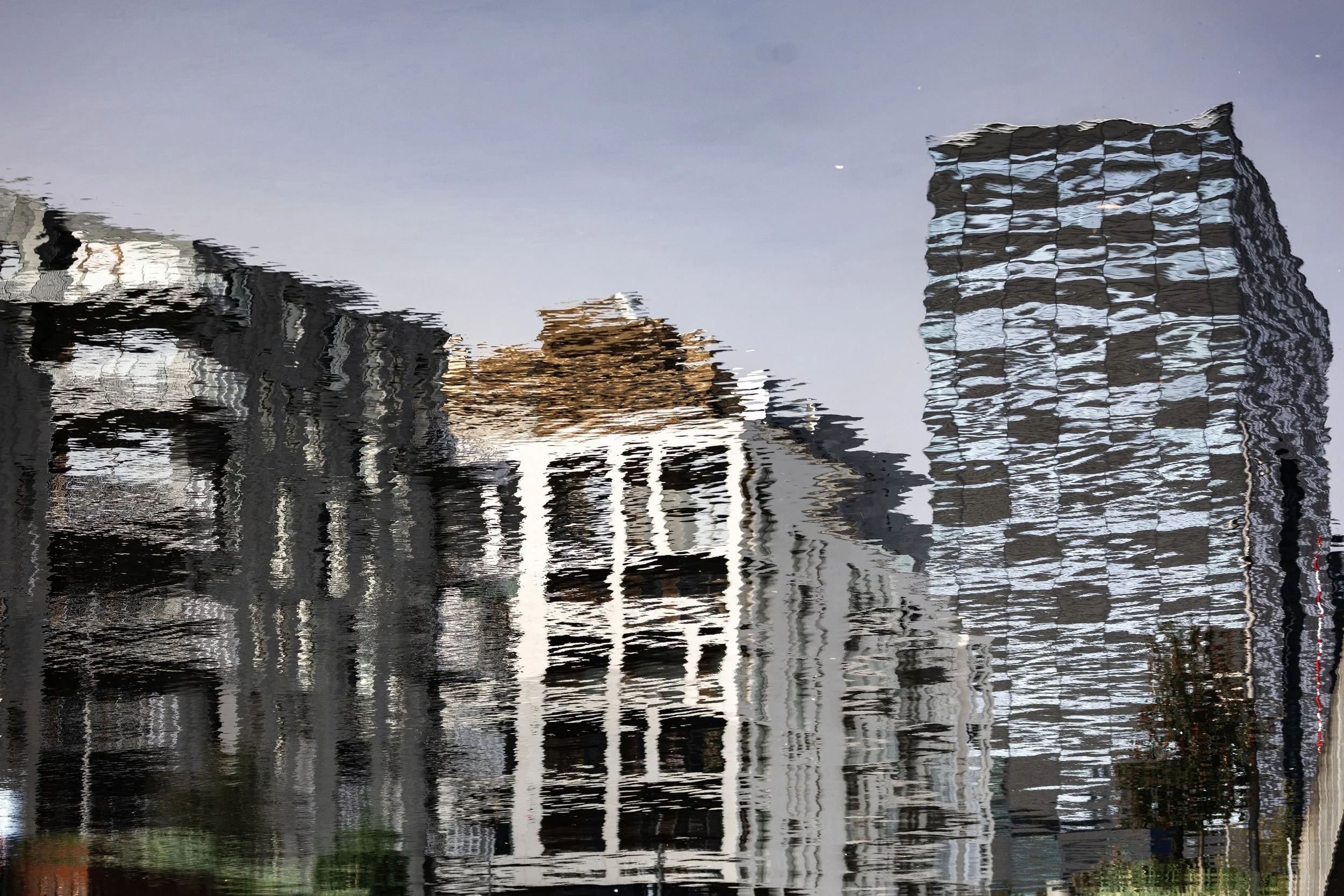 City buildings reflected upside down in rippled water with cream, black, and gold tones