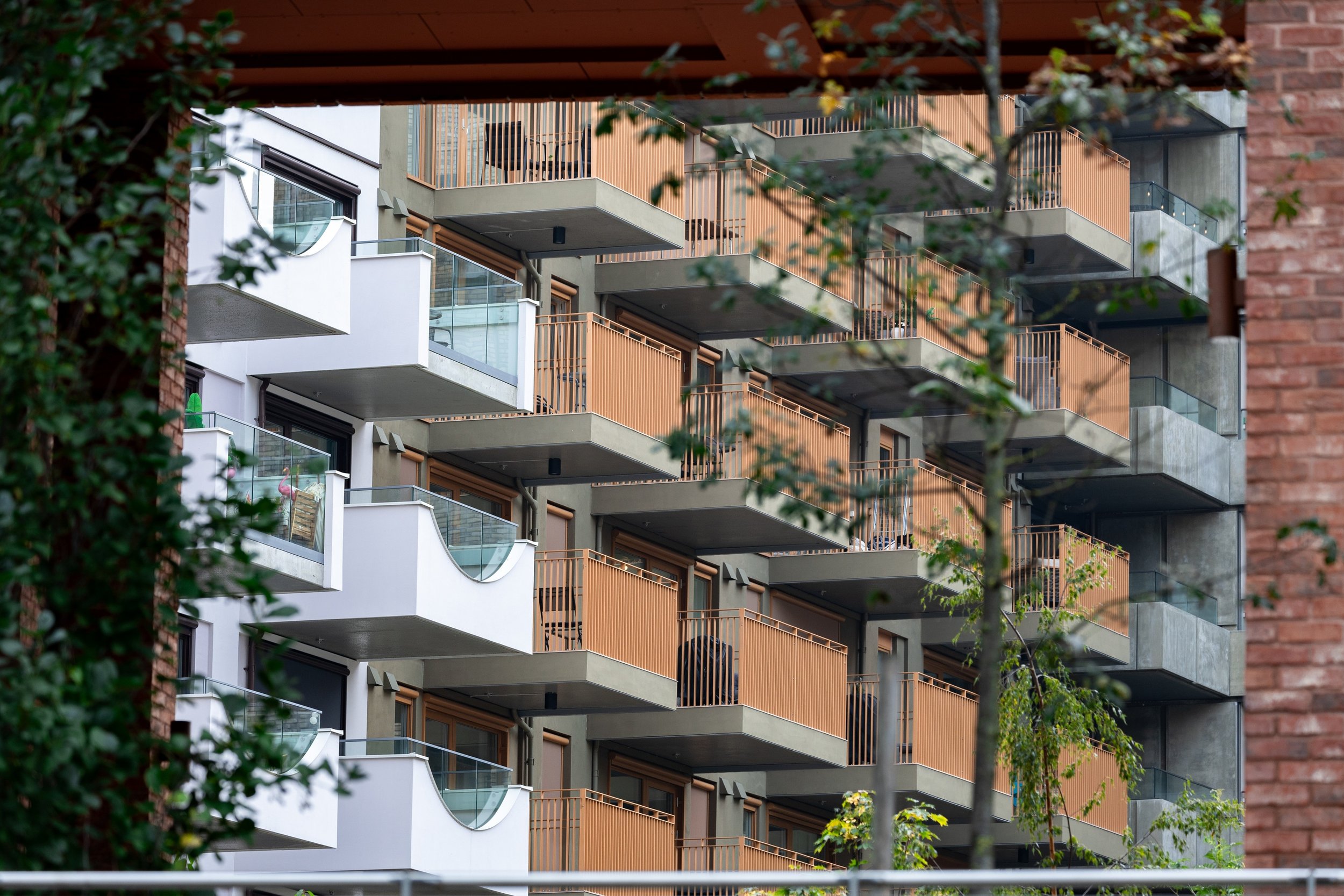 Repeating white and coral balconies across a brick facade framed by green foliage