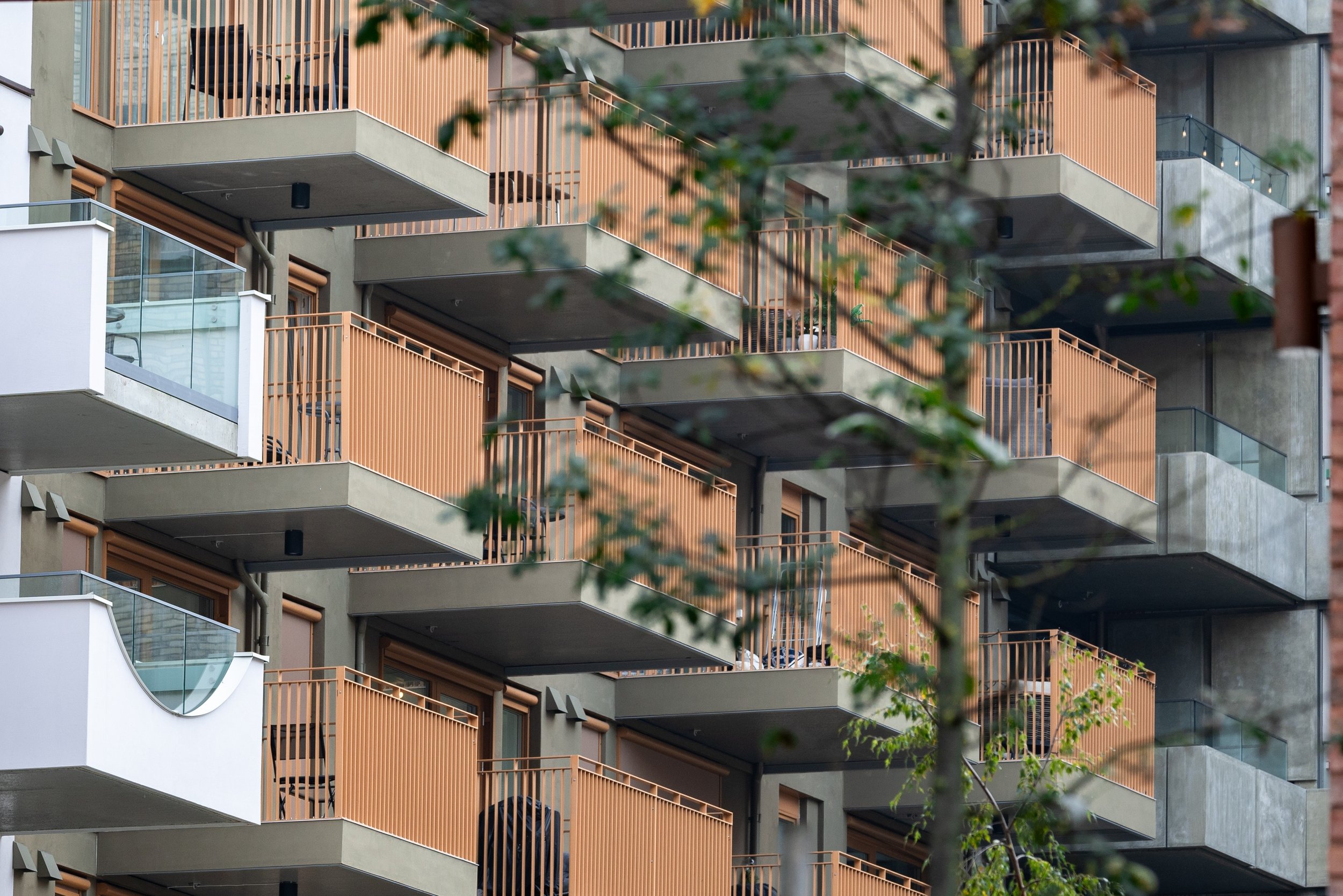 Close detail of rounded balcony railings, coral panels, windows, and brickwork