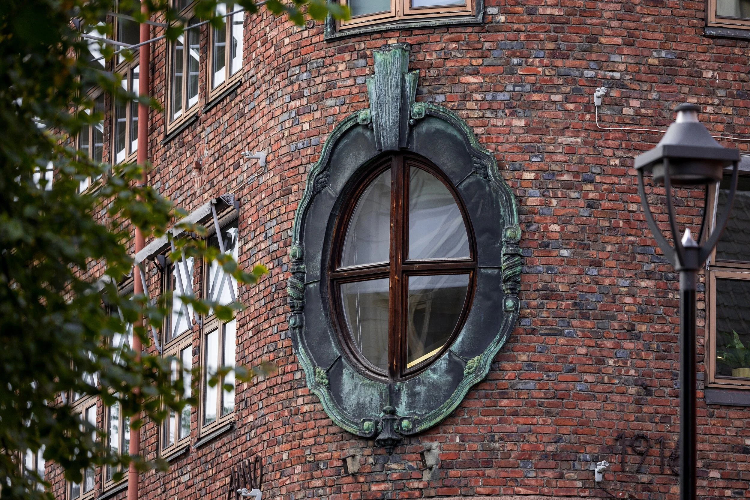 Oval wooden window in a weathered green metal surround on the corner of a red brick building
