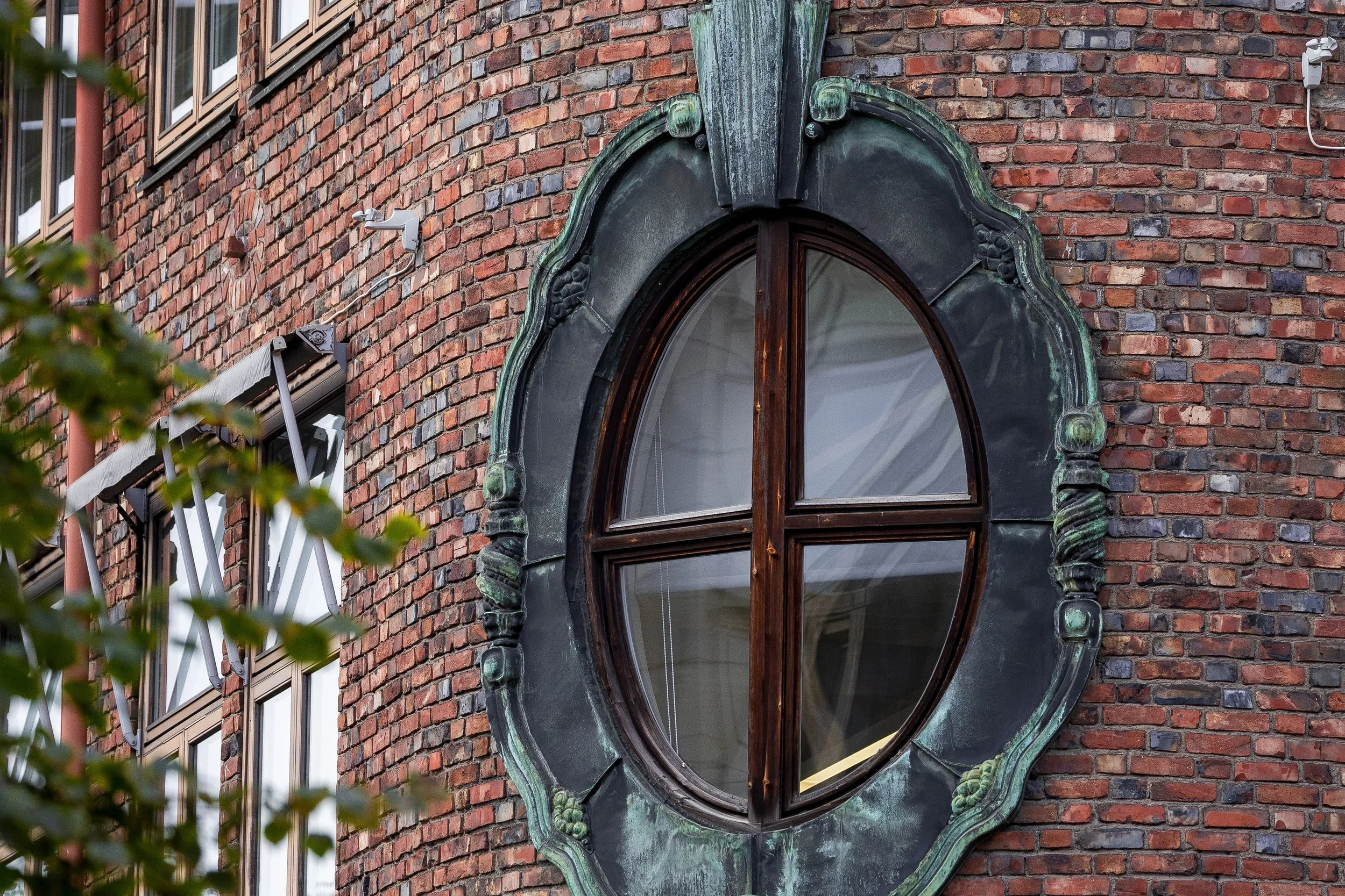 Close detail of the oval window, oxidized metal ornament, brickwork, leaves, and side windows