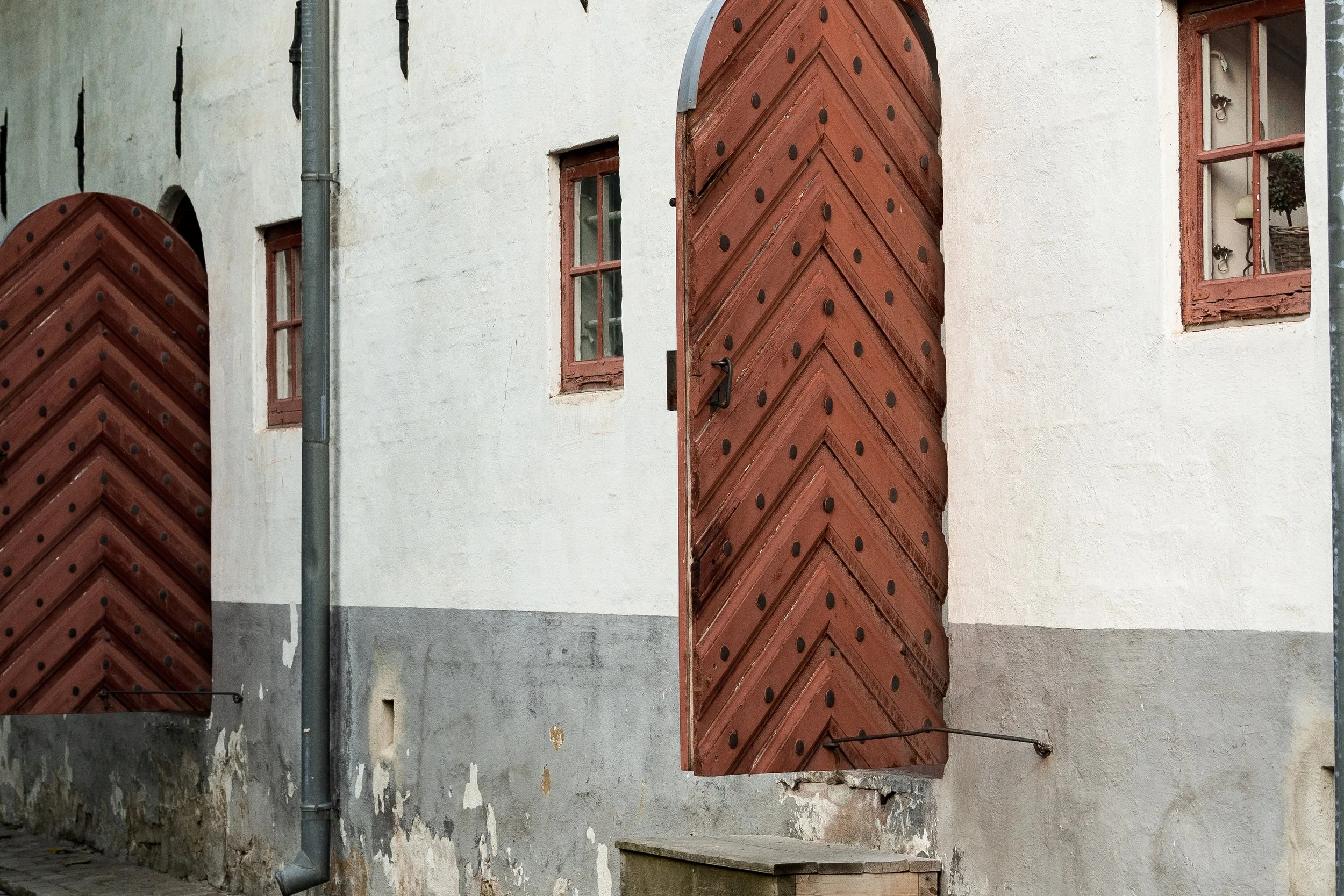 Close architectural detail of two red wooden doors, worn white plaster, stone steps, and a narrow window