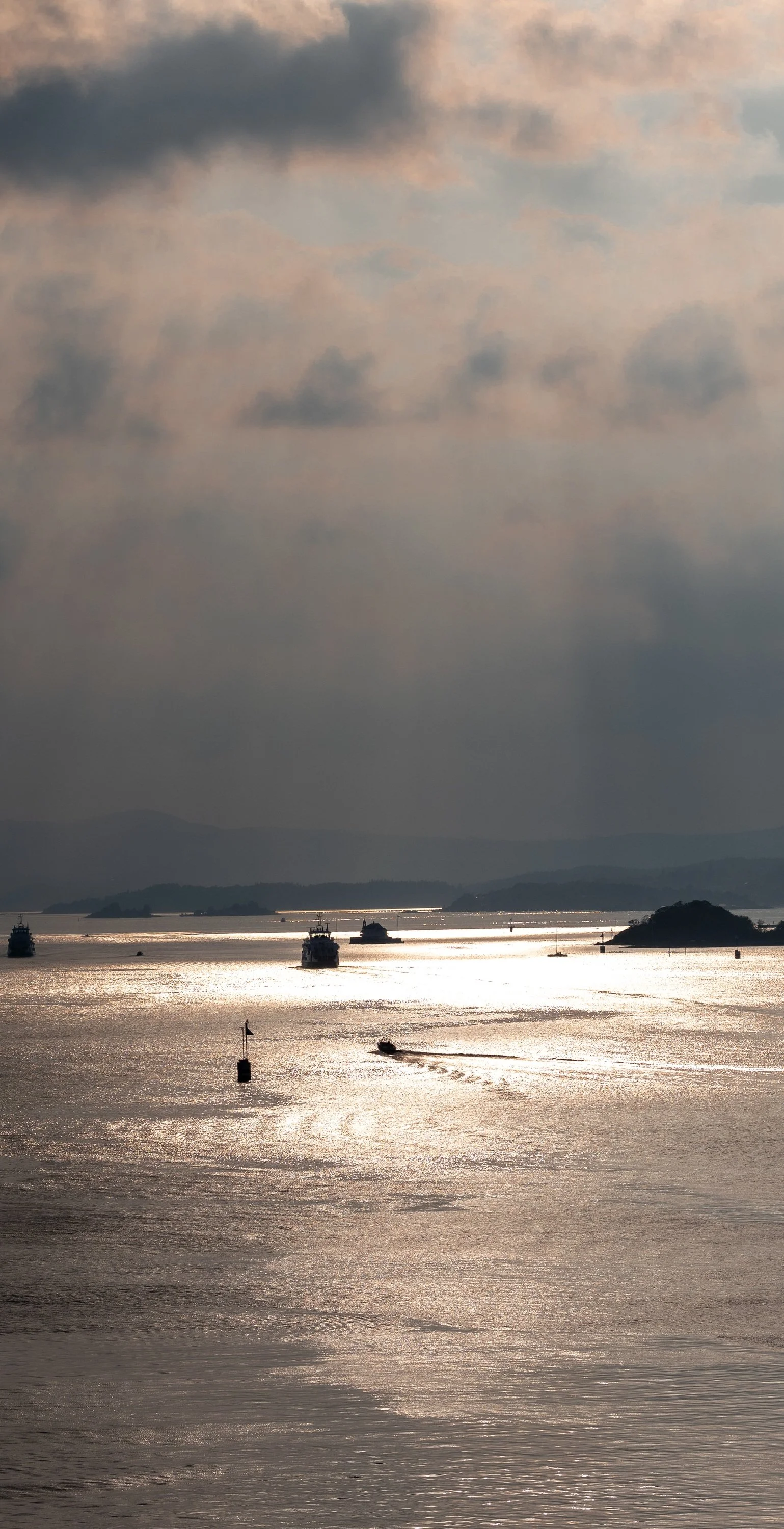 Close detail of sunlit water, distant boats, layered clouds, and shafts of light