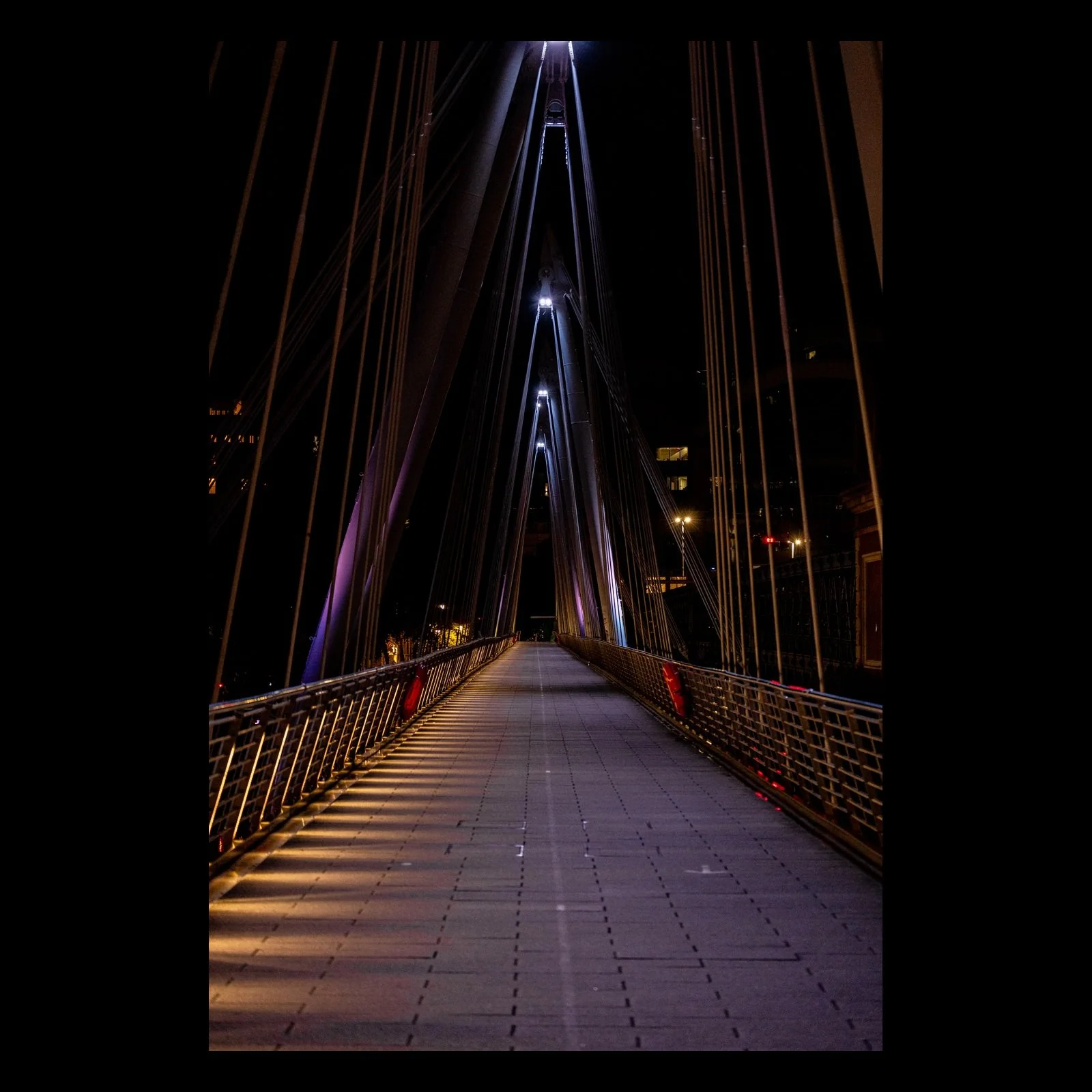 Electric Jubilee night suspension bridge photograph presented vertically against a black background