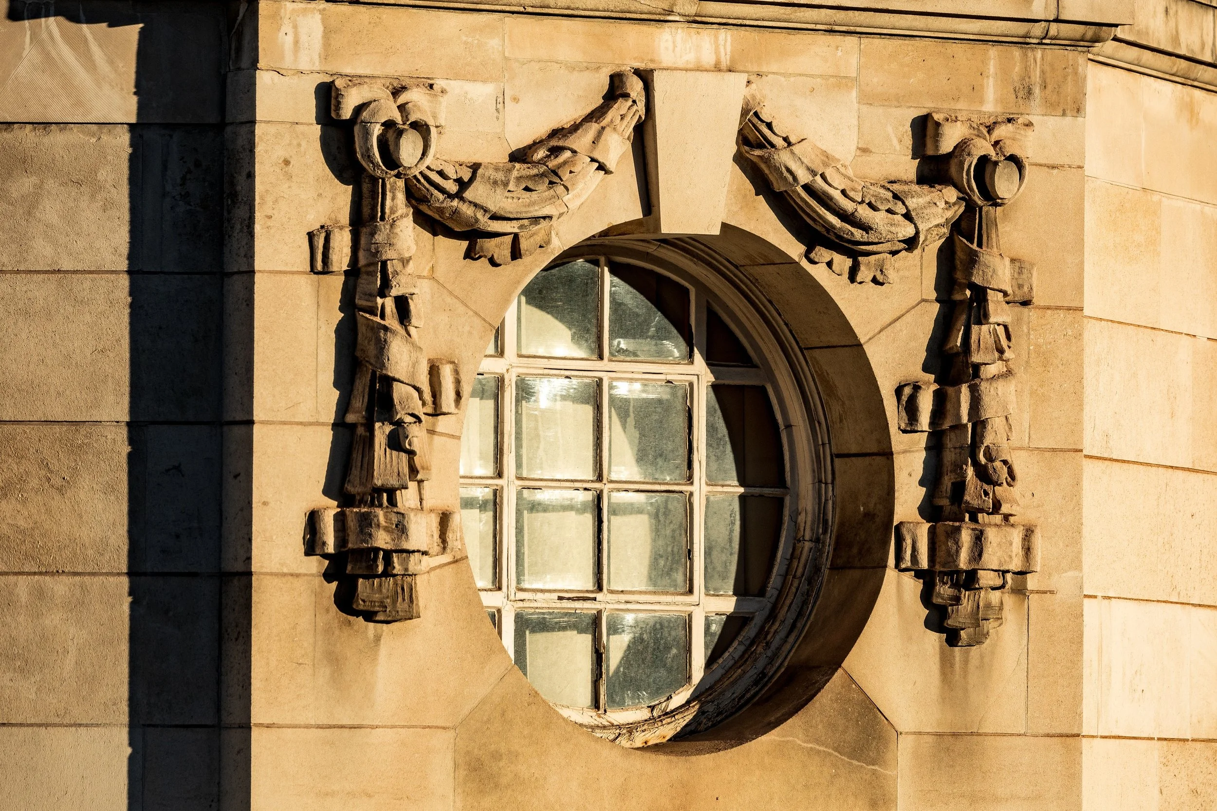 Circular multi-pane window surrounded by weathered stone figures and carved ornament in warm side light