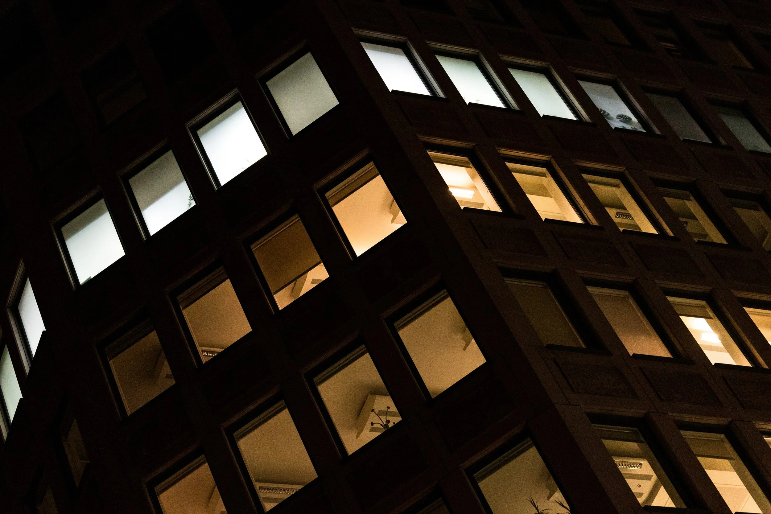 Upward tilted view of a London office facade with white and amber windows glowing at night