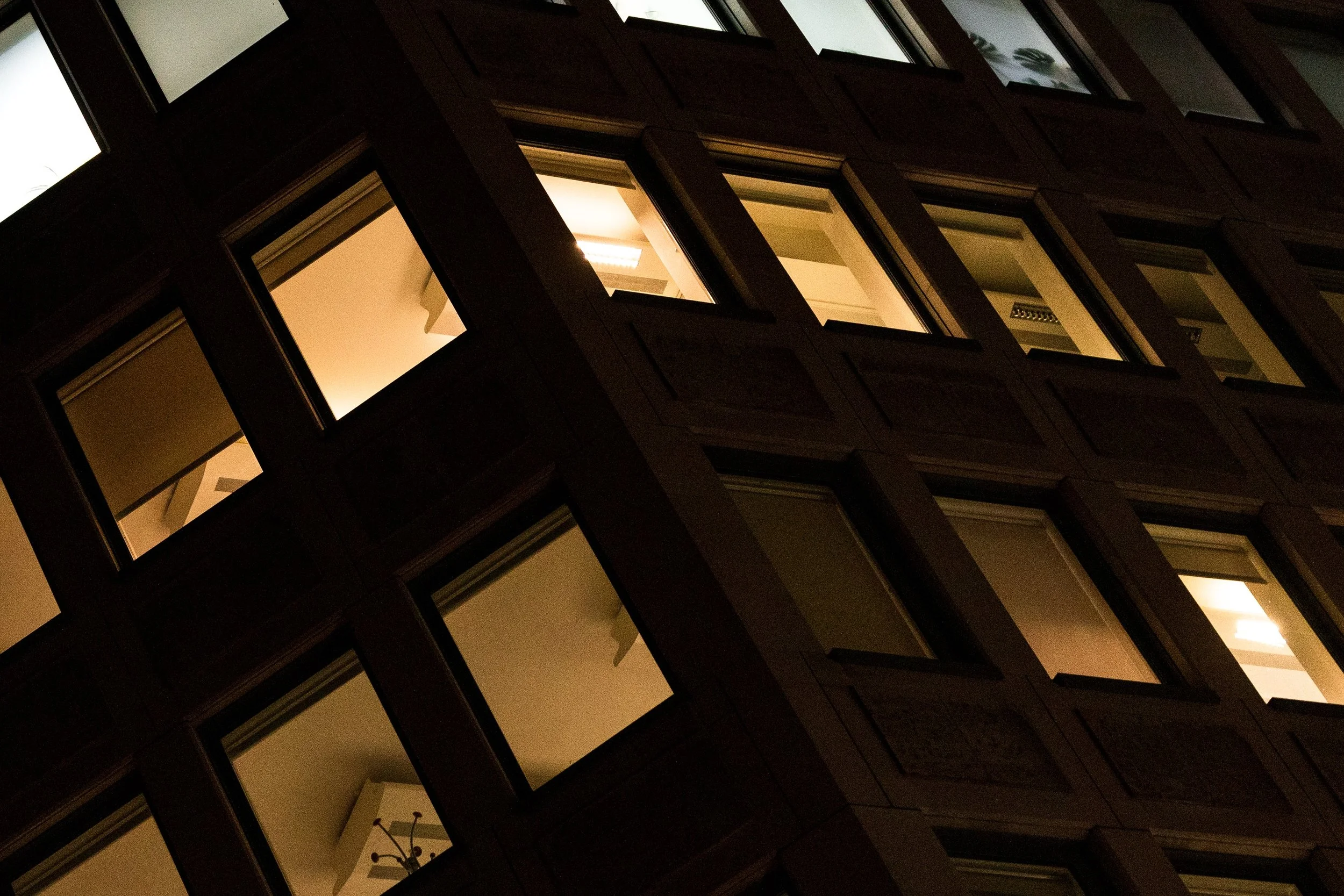 Close architectural detail of illuminated office windows divided by dark diagonal frames