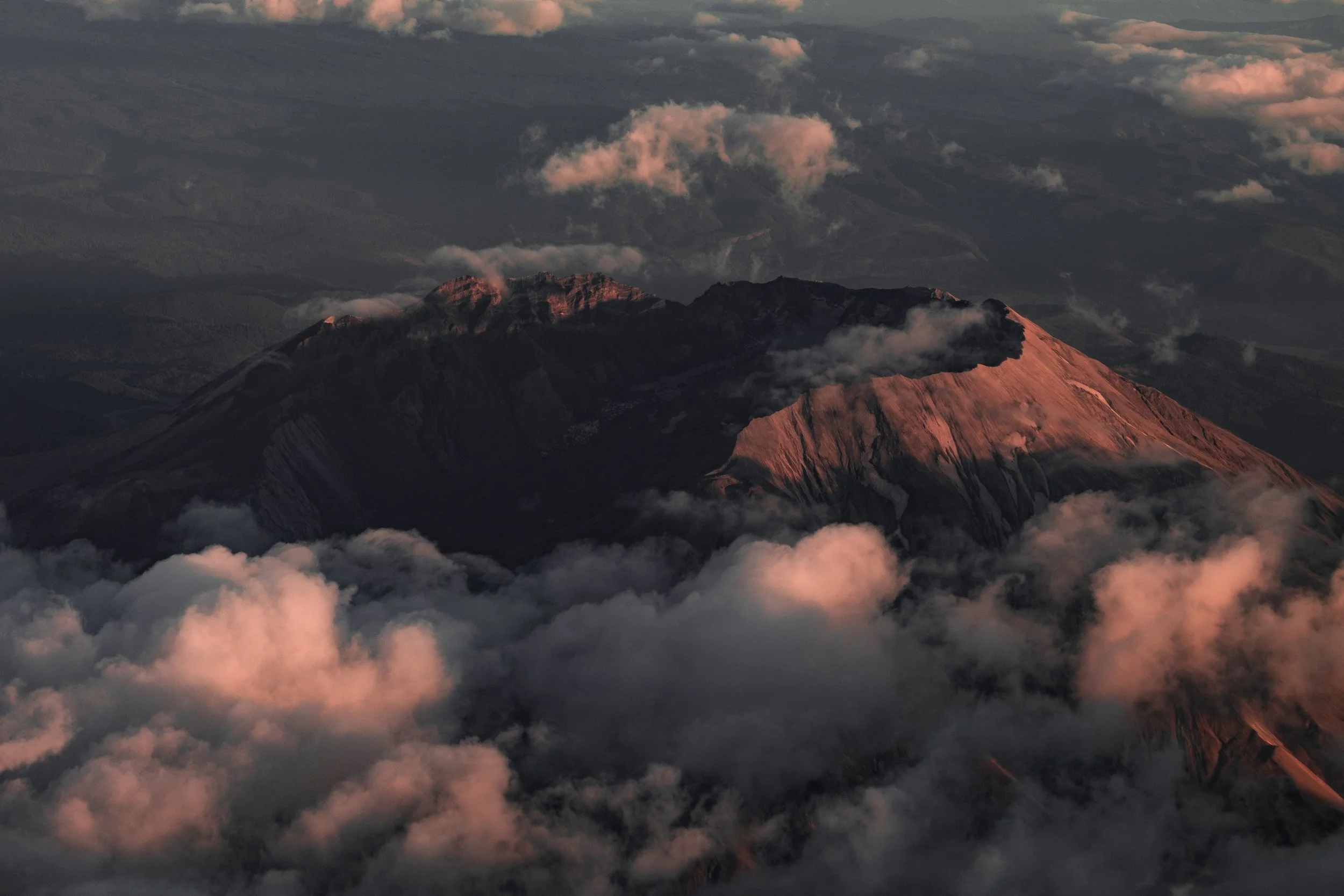 Mount St. Helens crater rising above clouds with warm evening light across one volcanic slope