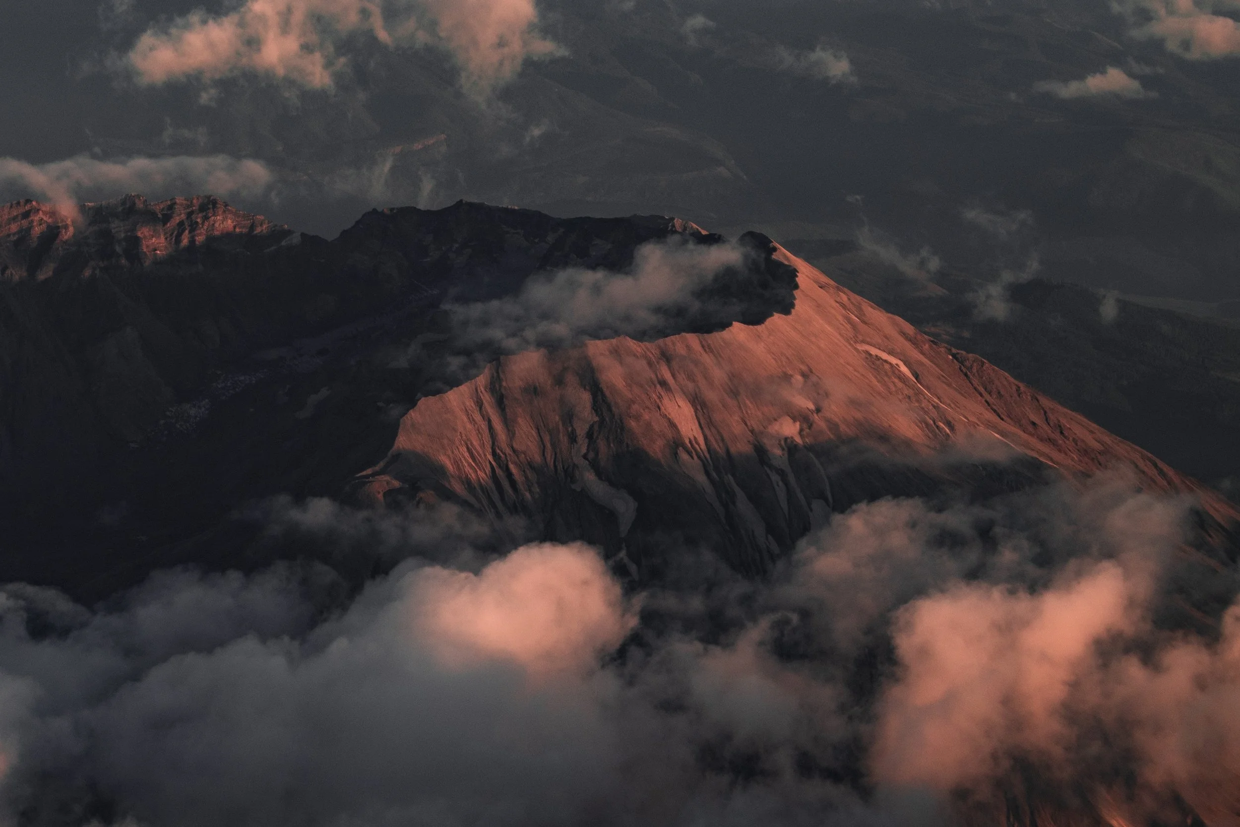 Close detail of the shadowed crater, illuminated ridges, and rose-colored clouds around Mount St. Helens