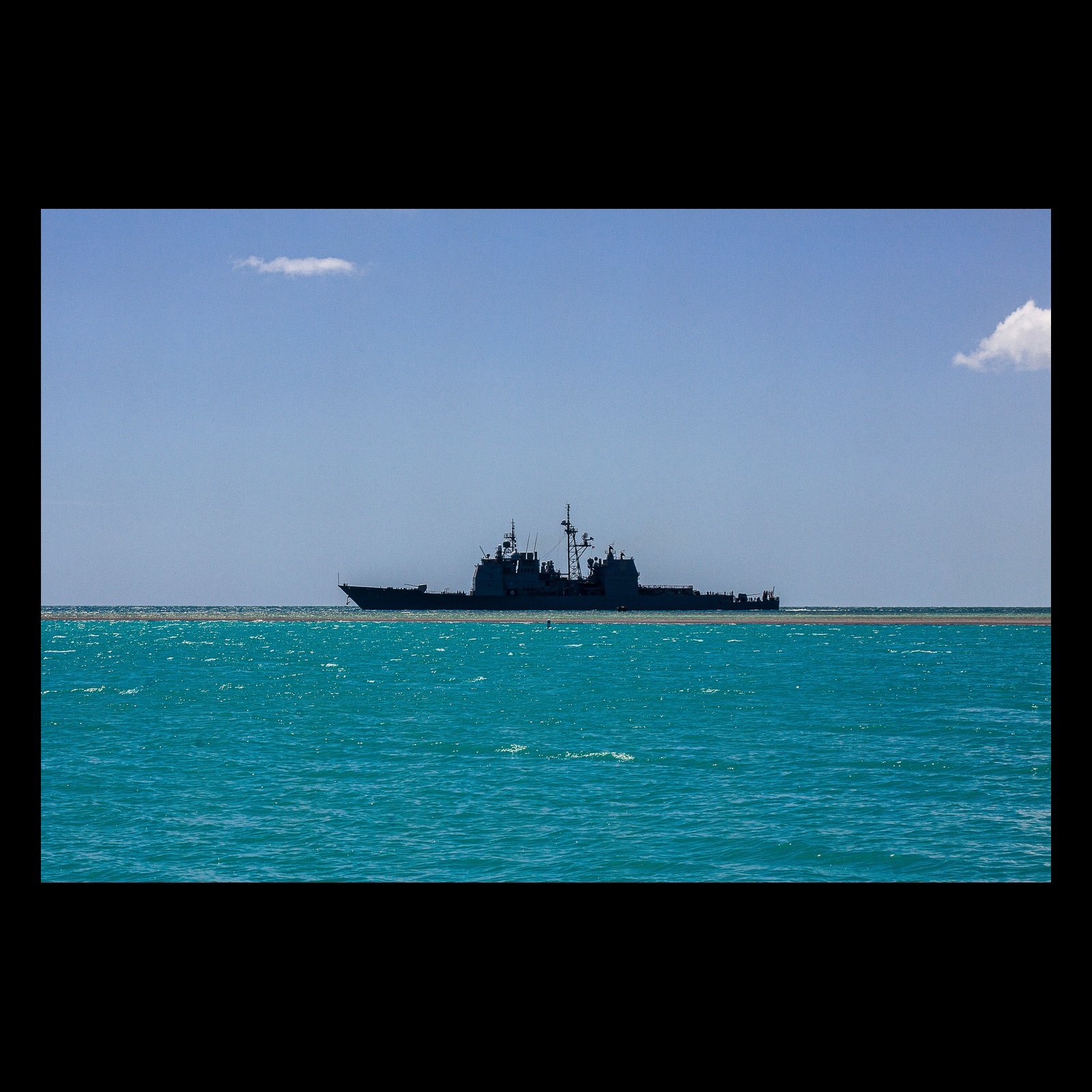 Full-frame black presentation thumbnail of Pacific Sentinel, showing a dark naval vessel crosses clear turquoise water beneath a spare blue sky